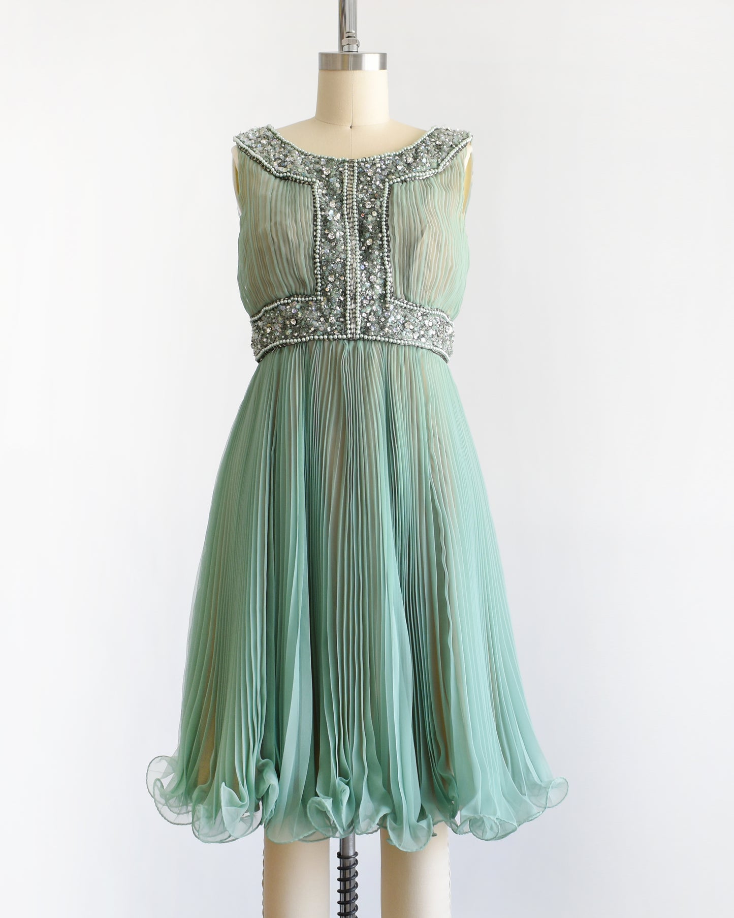 a vintage 1960s green chiffon dress with beaded neckline and bodice on a mannequin against a white background