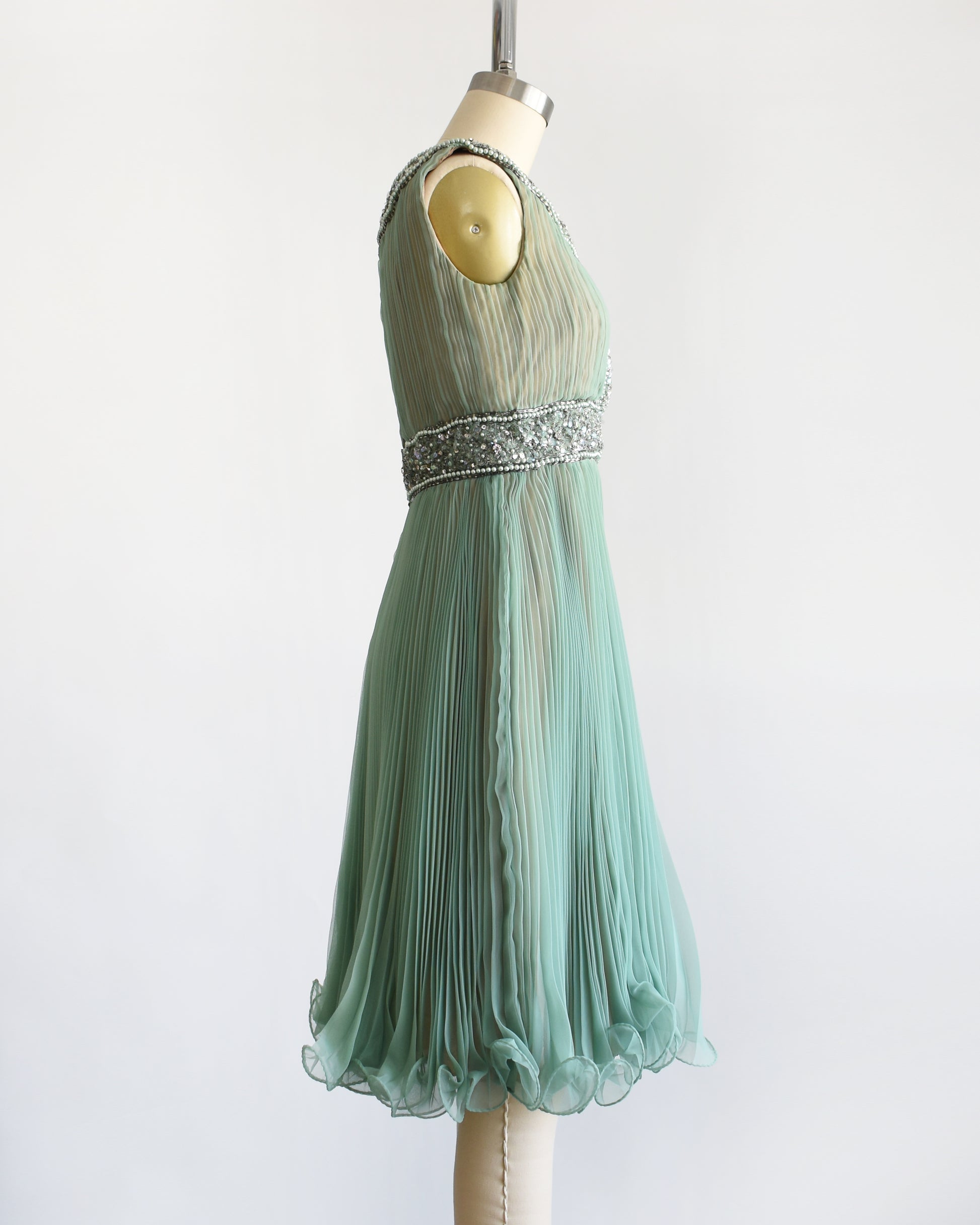 side view of a vintage 1960s green chiffon dress with beaded neckline and bodice on a mannequin against a white background