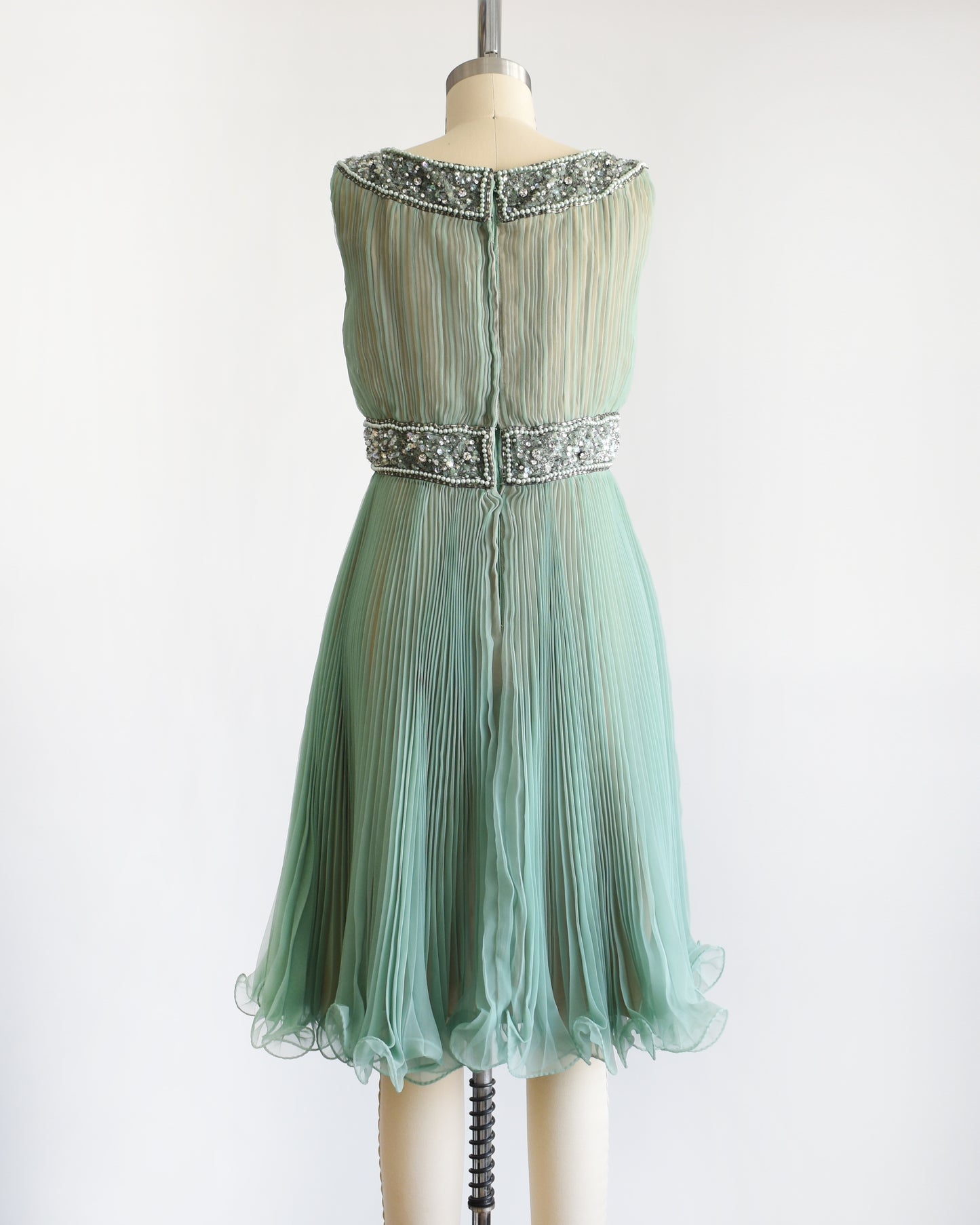 back view of a vintage 1960s green chiffon dress with beaded neckline and bodice on a mannequin against a white background