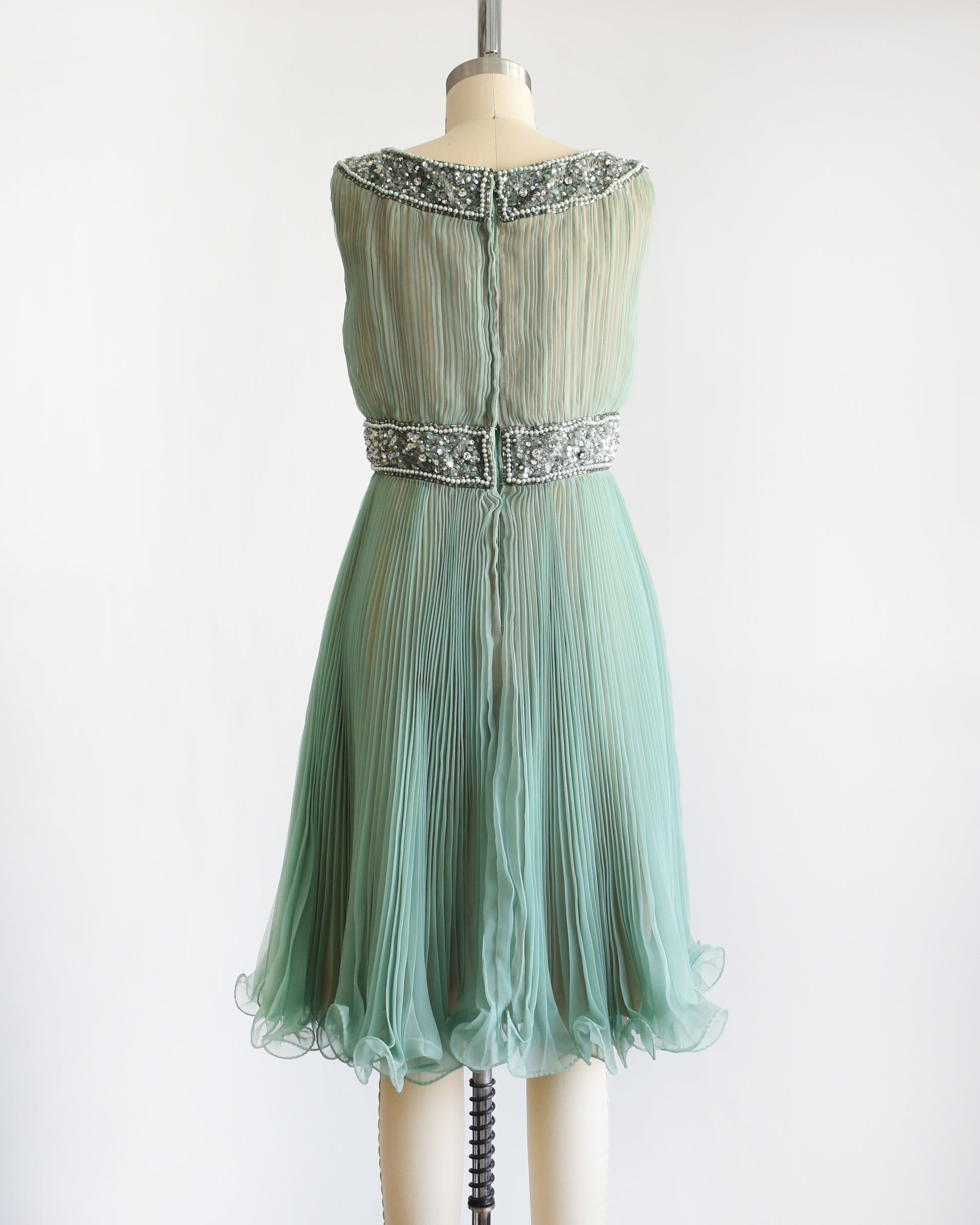 back view of a vintage 1960s green chiffon dress with beaded neckline and bodice on a mannequin against a white background