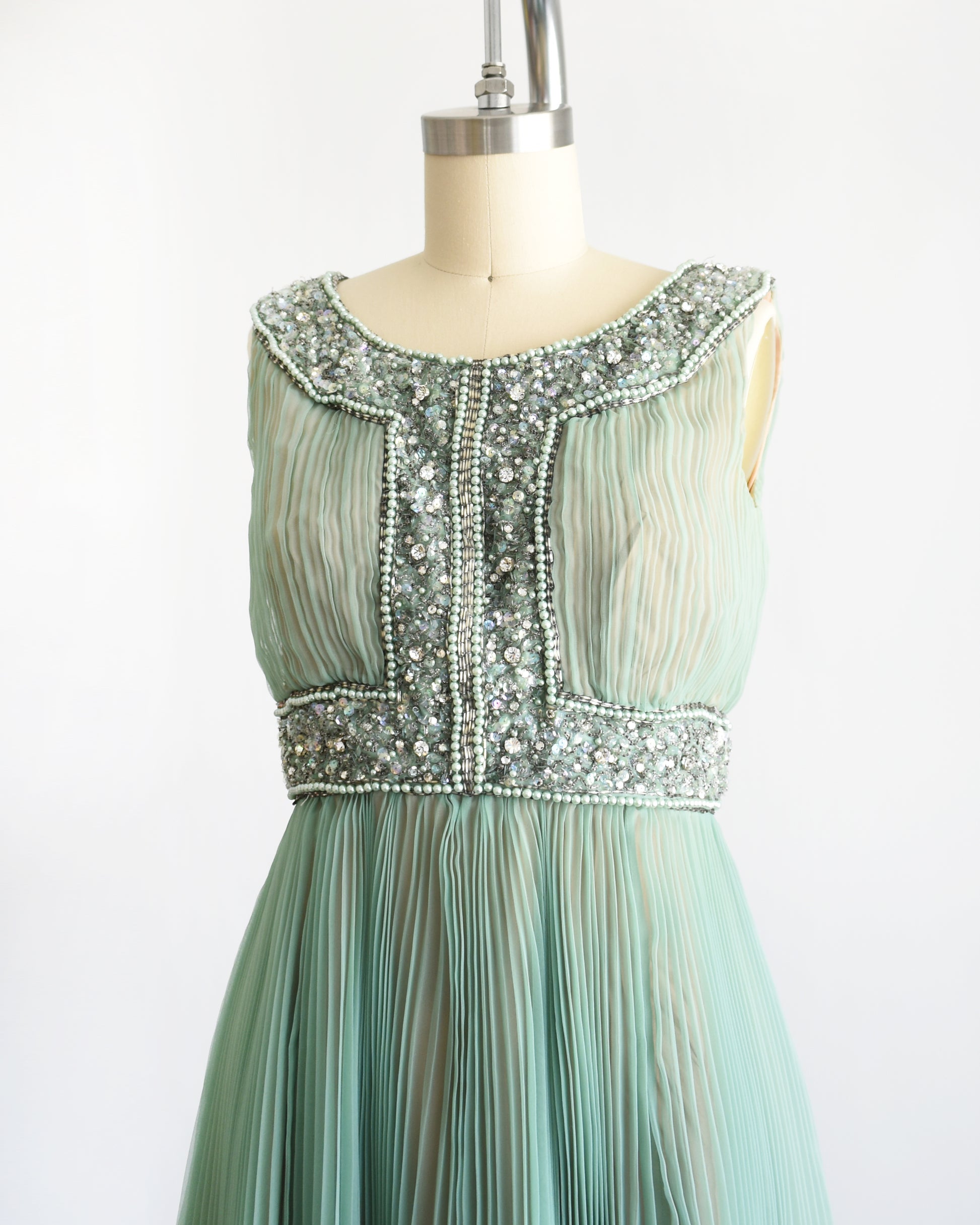 side front view of a vintage 1960s green chiffon dress with beaded neckline and bodice on a mannequin against a white background
