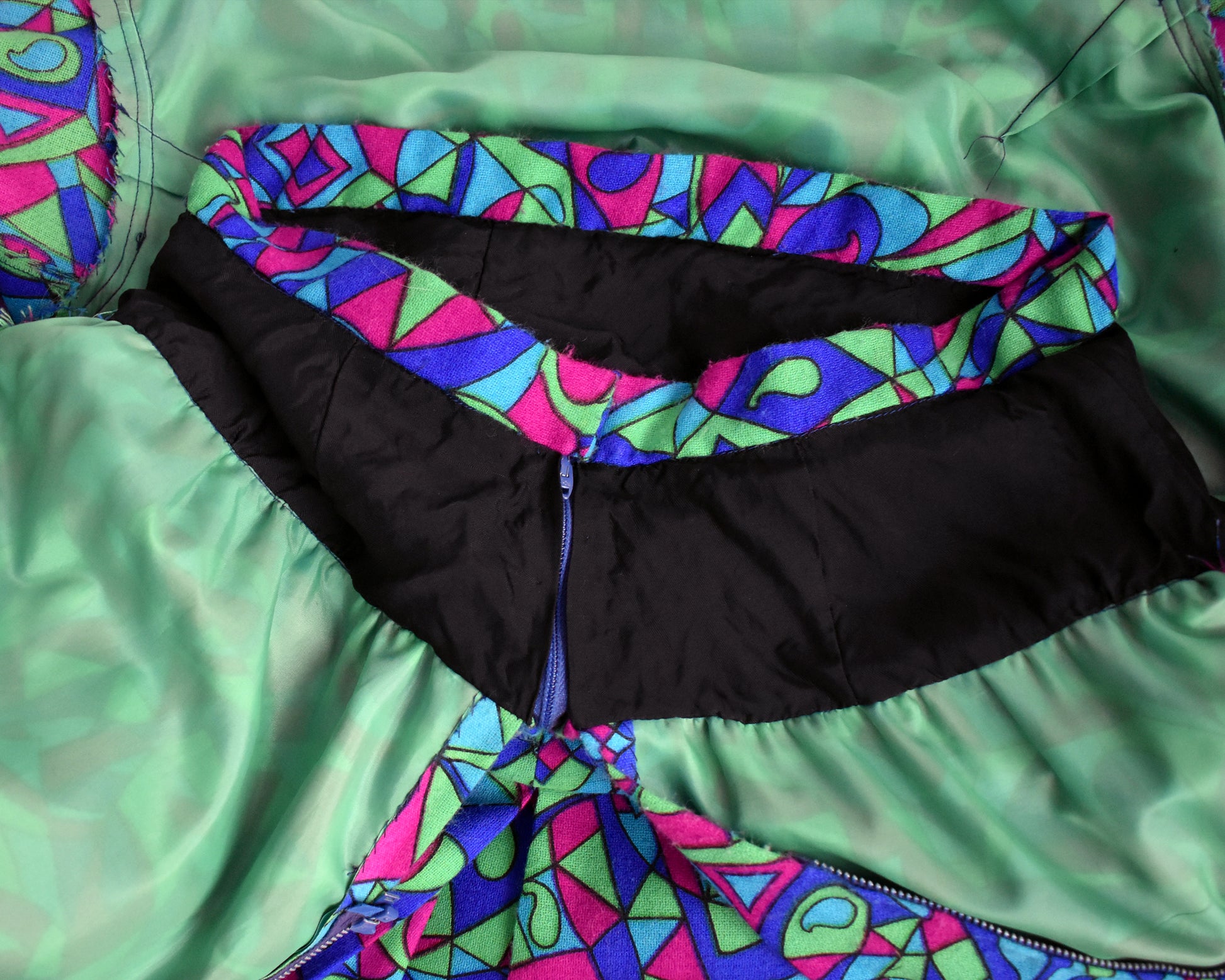 close up of the inside waistband of the skirt on a vintage 1960s psychedelic patterned dress on a mannequin against a white background