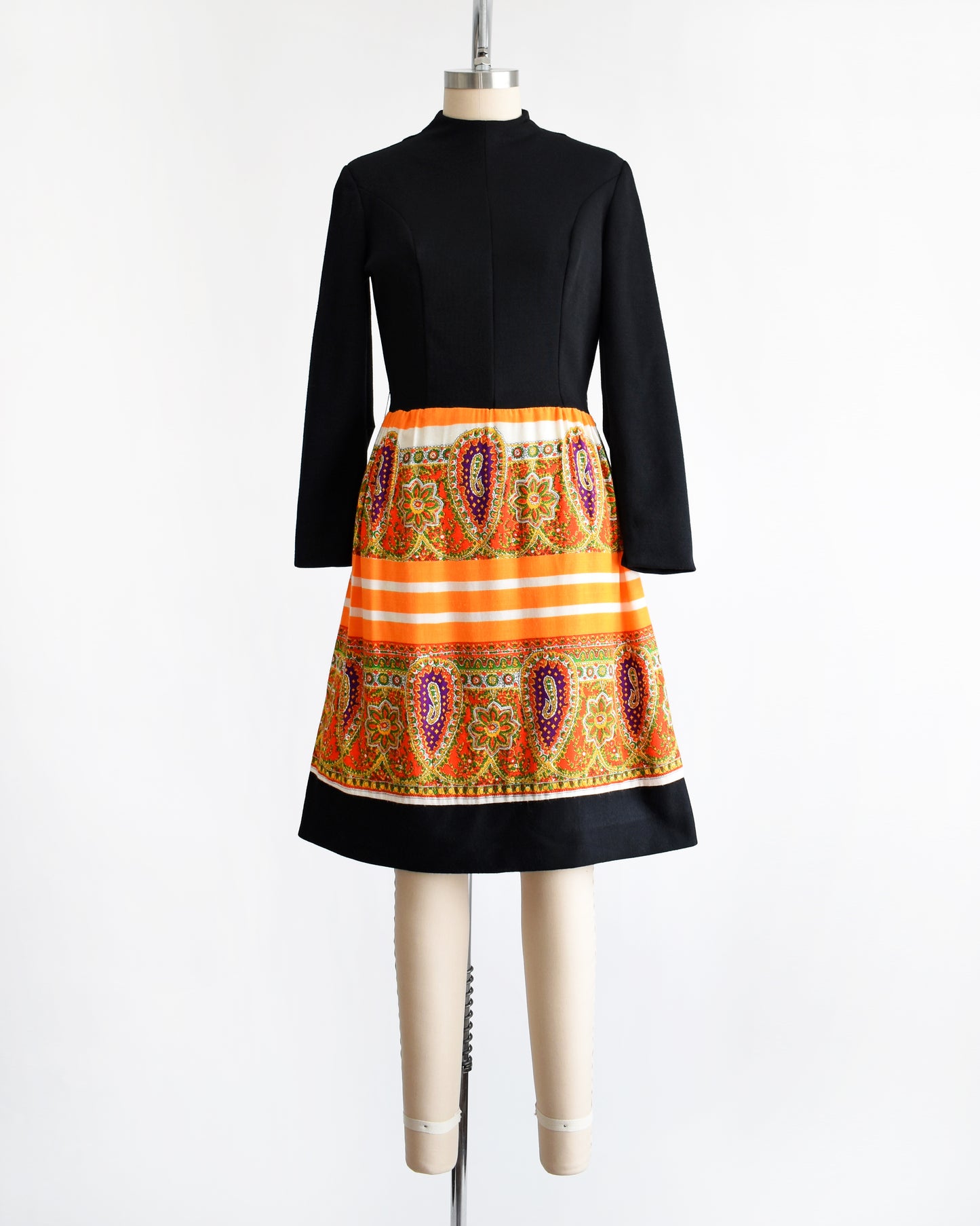 a vintage 1960s black and orange dress with a colorful patterned skirt on a mannequin against a white background