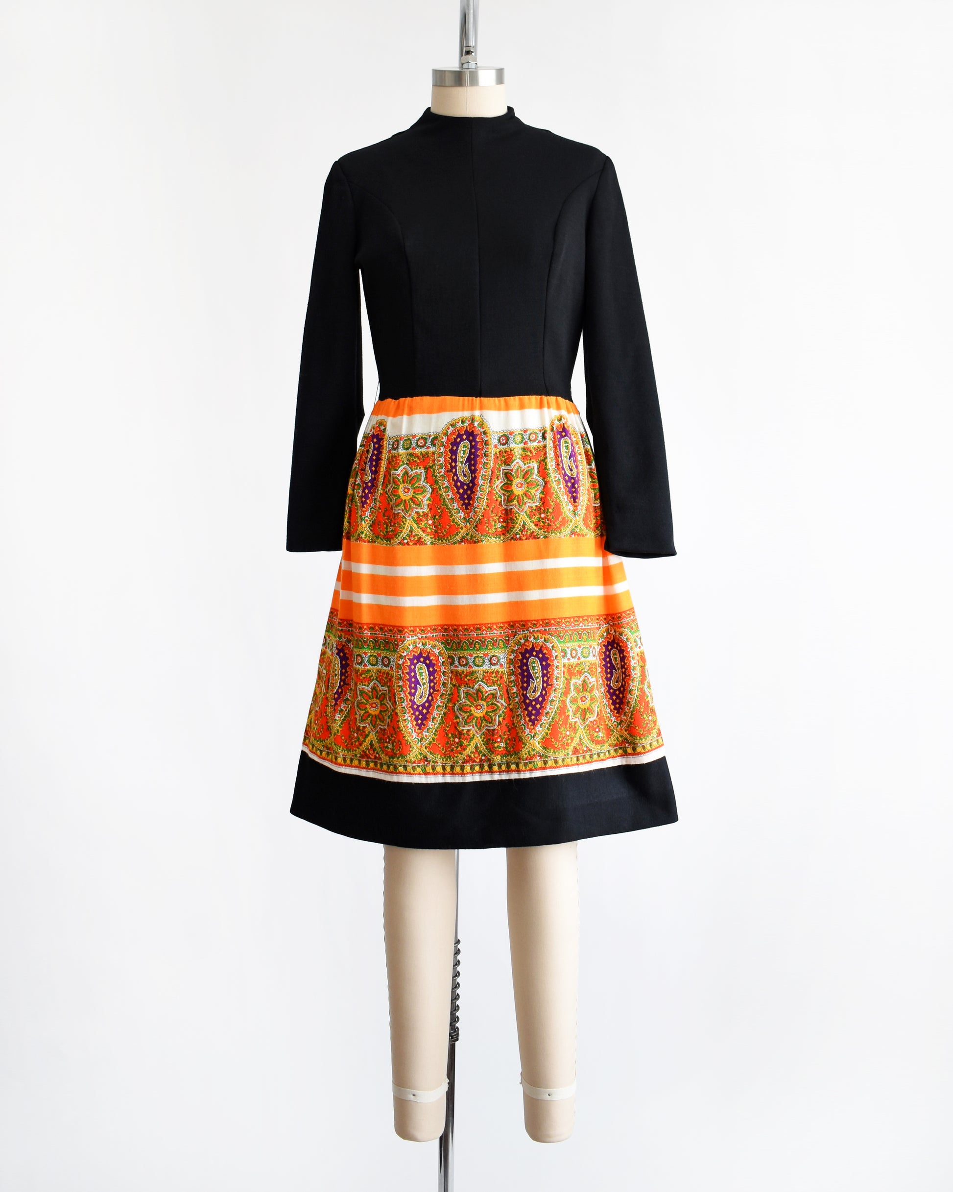 a vintage 1960s black and orange dress with a colorful patterned skirt on a mannequin against a white background