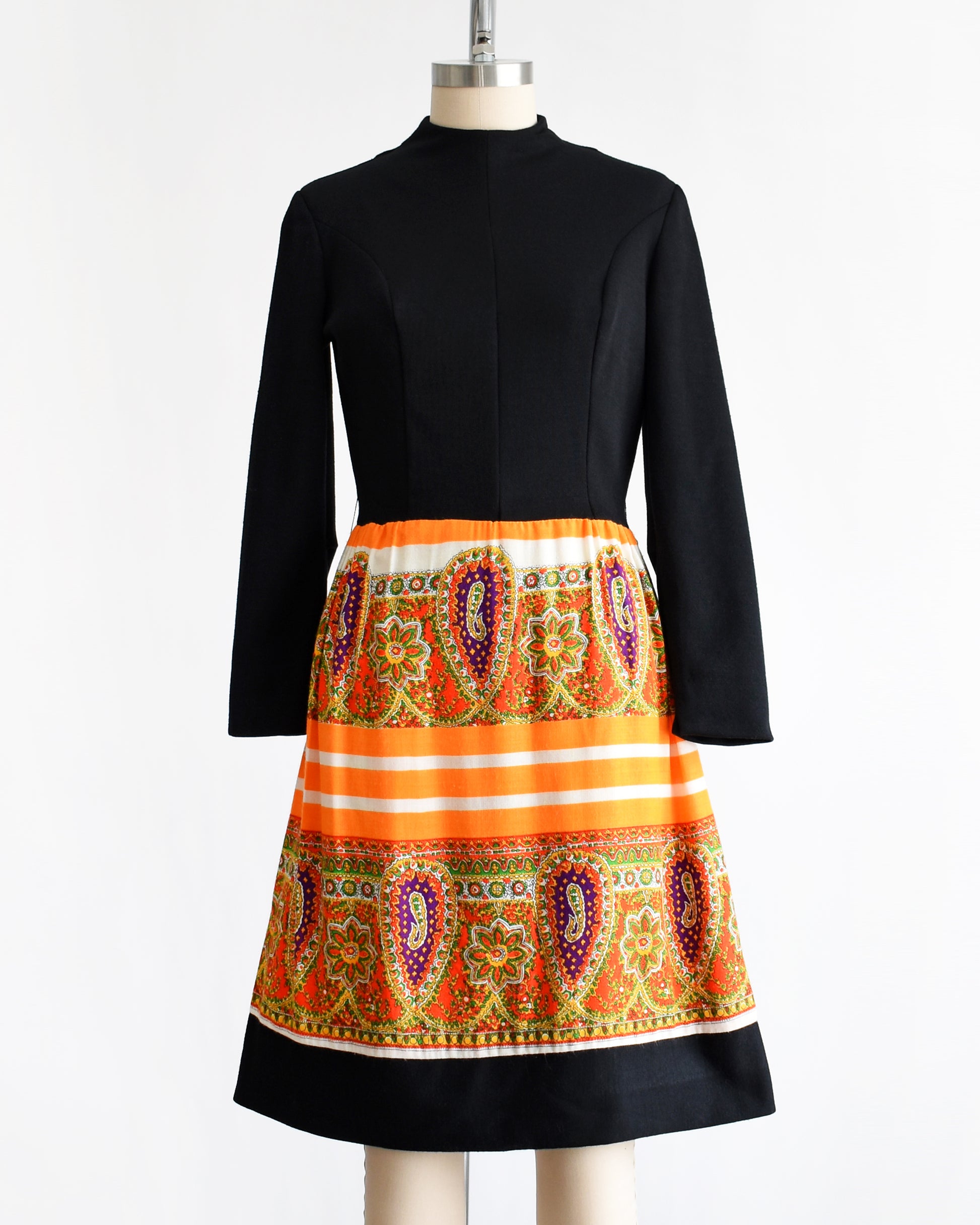 a vintage 1960s black and orange dress with a colorful patterned skirt on a mannequin against a white background