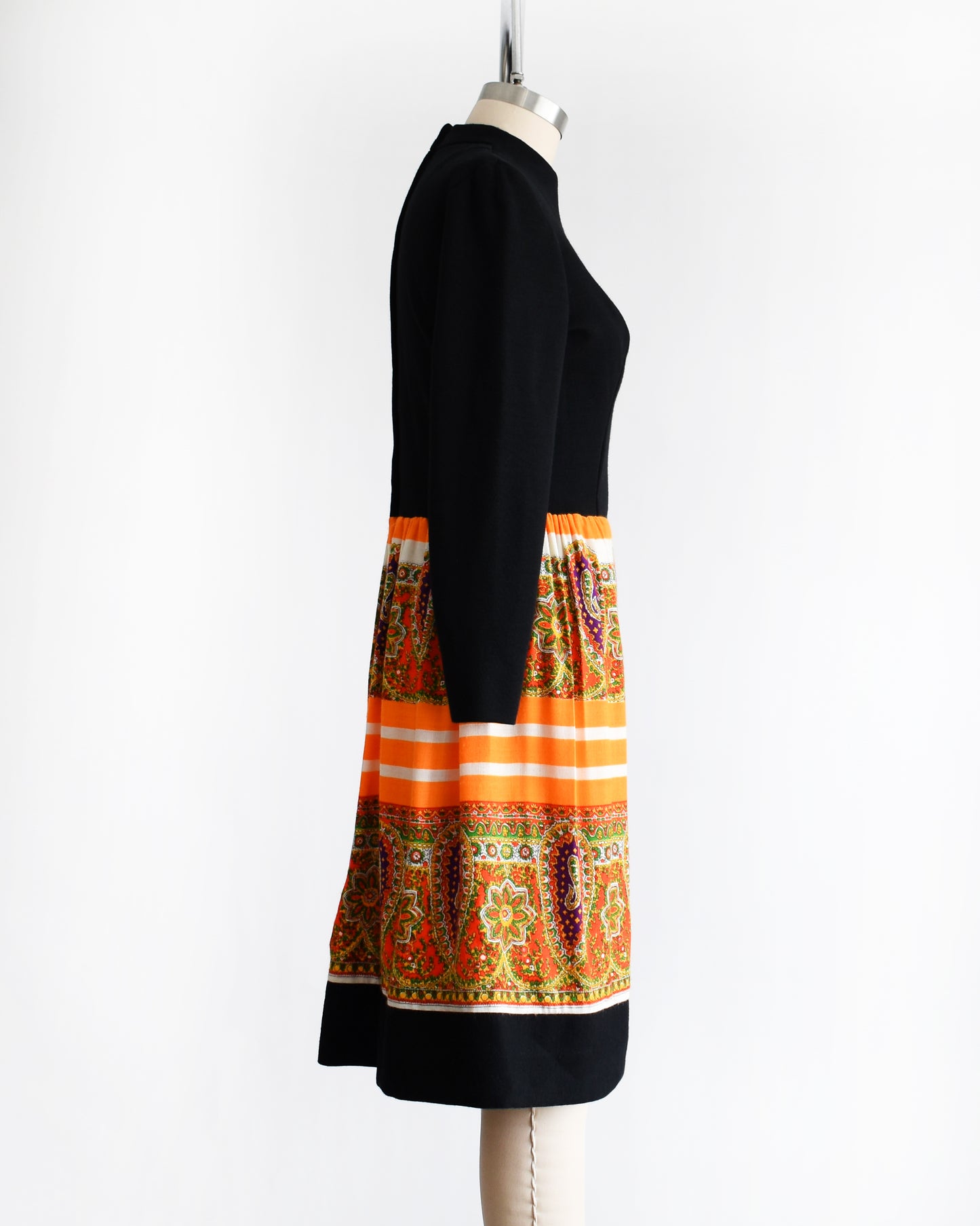 side view of a vintage 1960s black and orange dress with a colorful patterned skirt on a mannequin against a white background