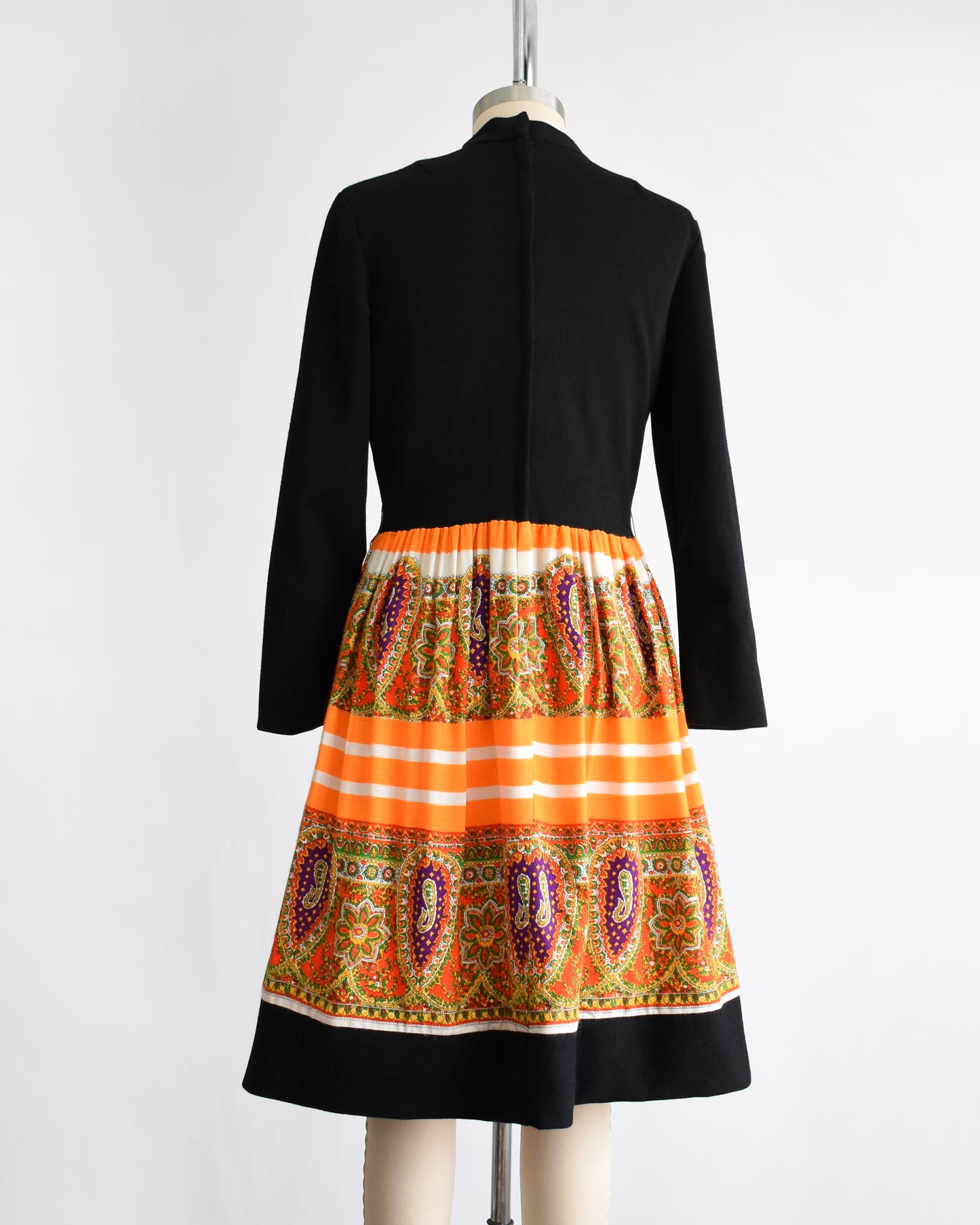 back view of a vintage 1960s black and orange dress with a colorful patterned skirt on a mannequin against a white background