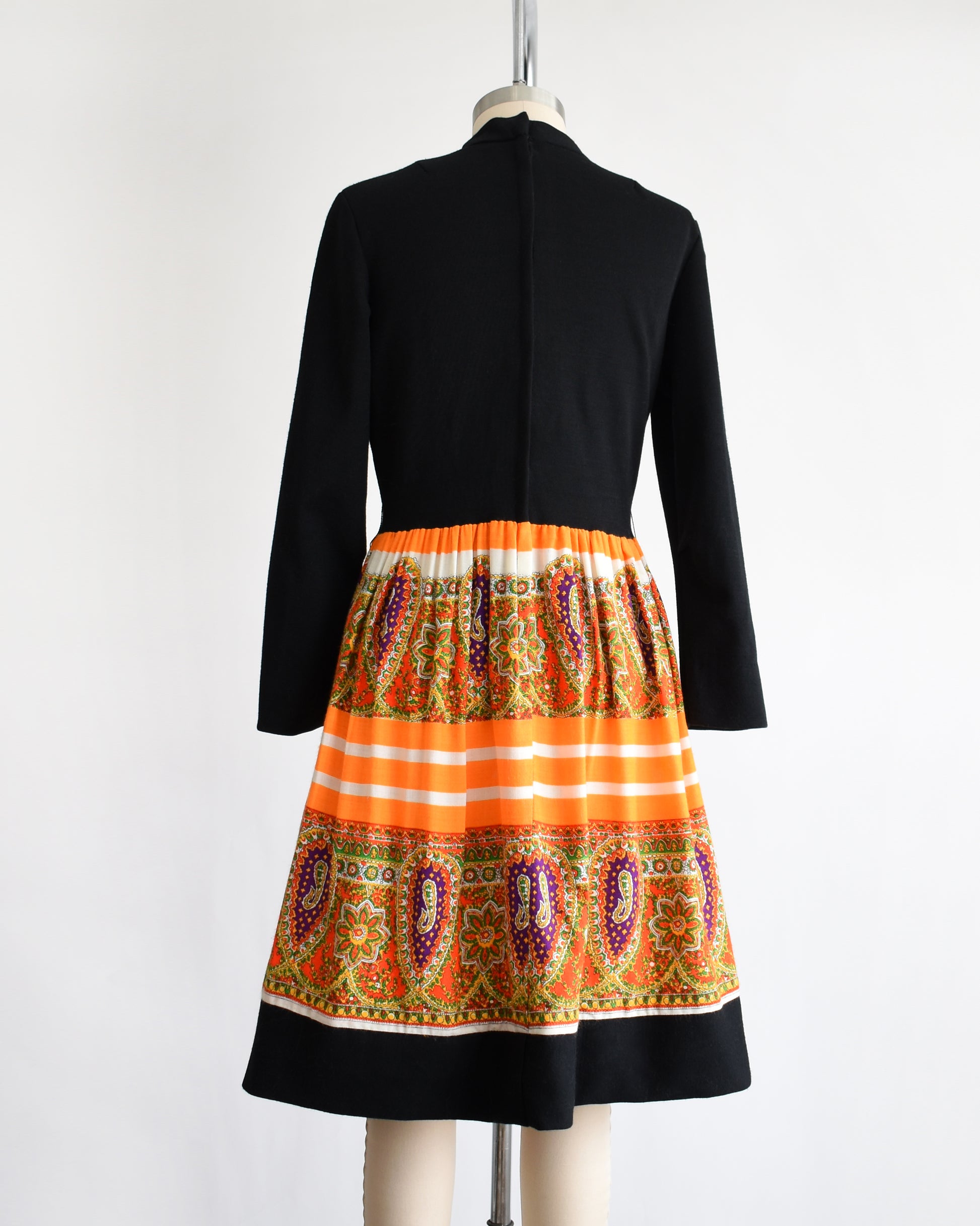 back view of a vintage 1960s black and orange dress with a colorful patterned skirt on a mannequin against a white background