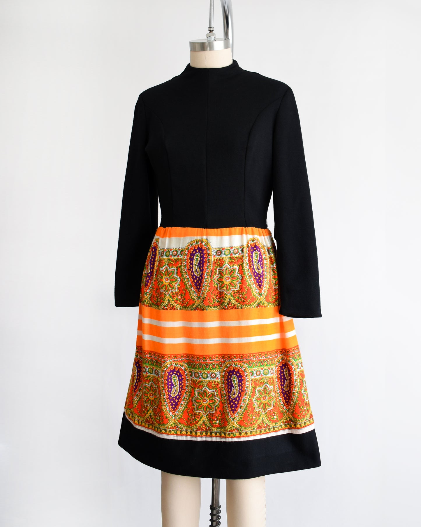 side front view of a vintage 1960s black and orange dress with a colorful patterned skirt on a mannequin against a white background