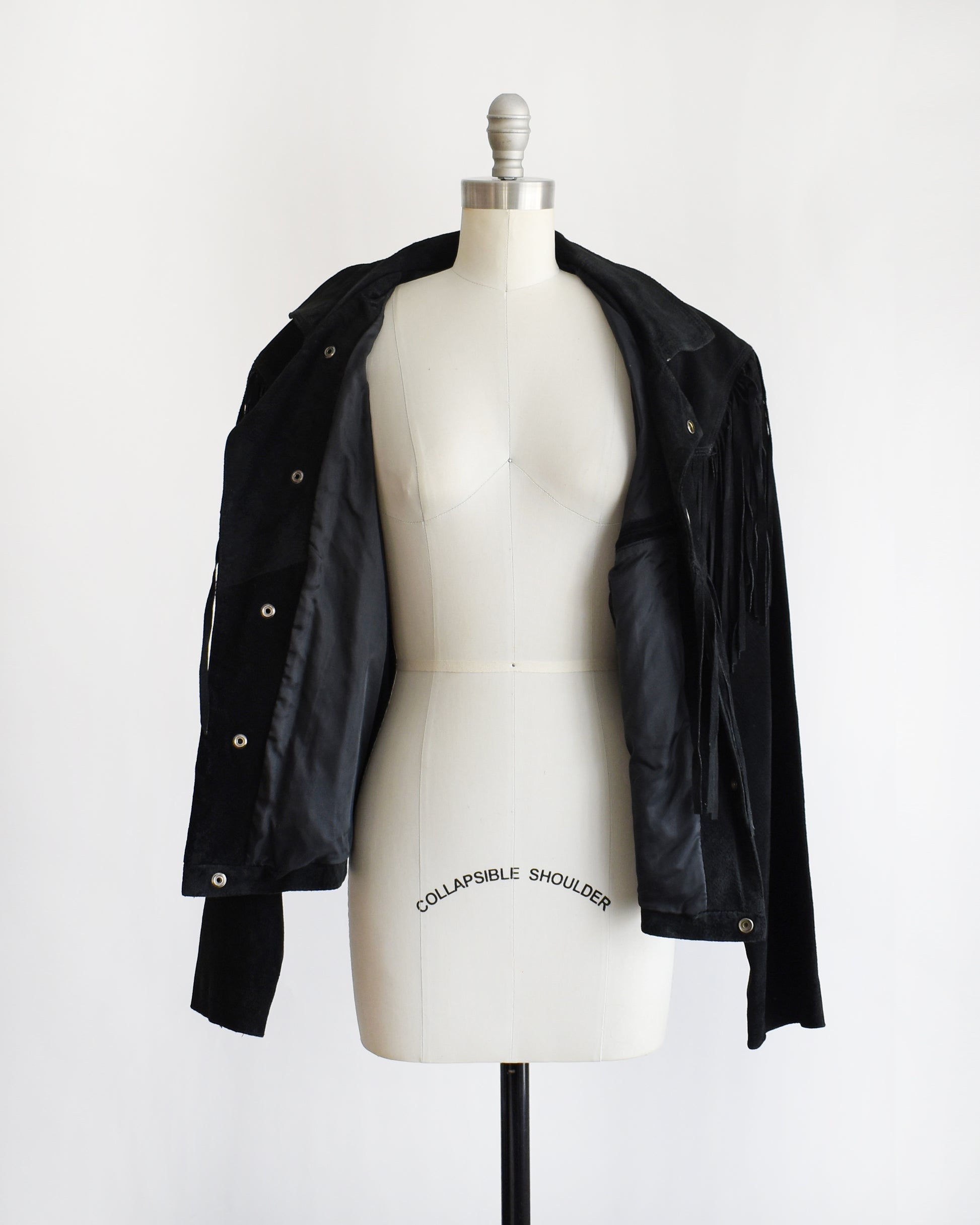 a vintage 1990s black fringed jacket on a mannequin against a white background. the coat is unbuttoned and opened showing the black lining inside.