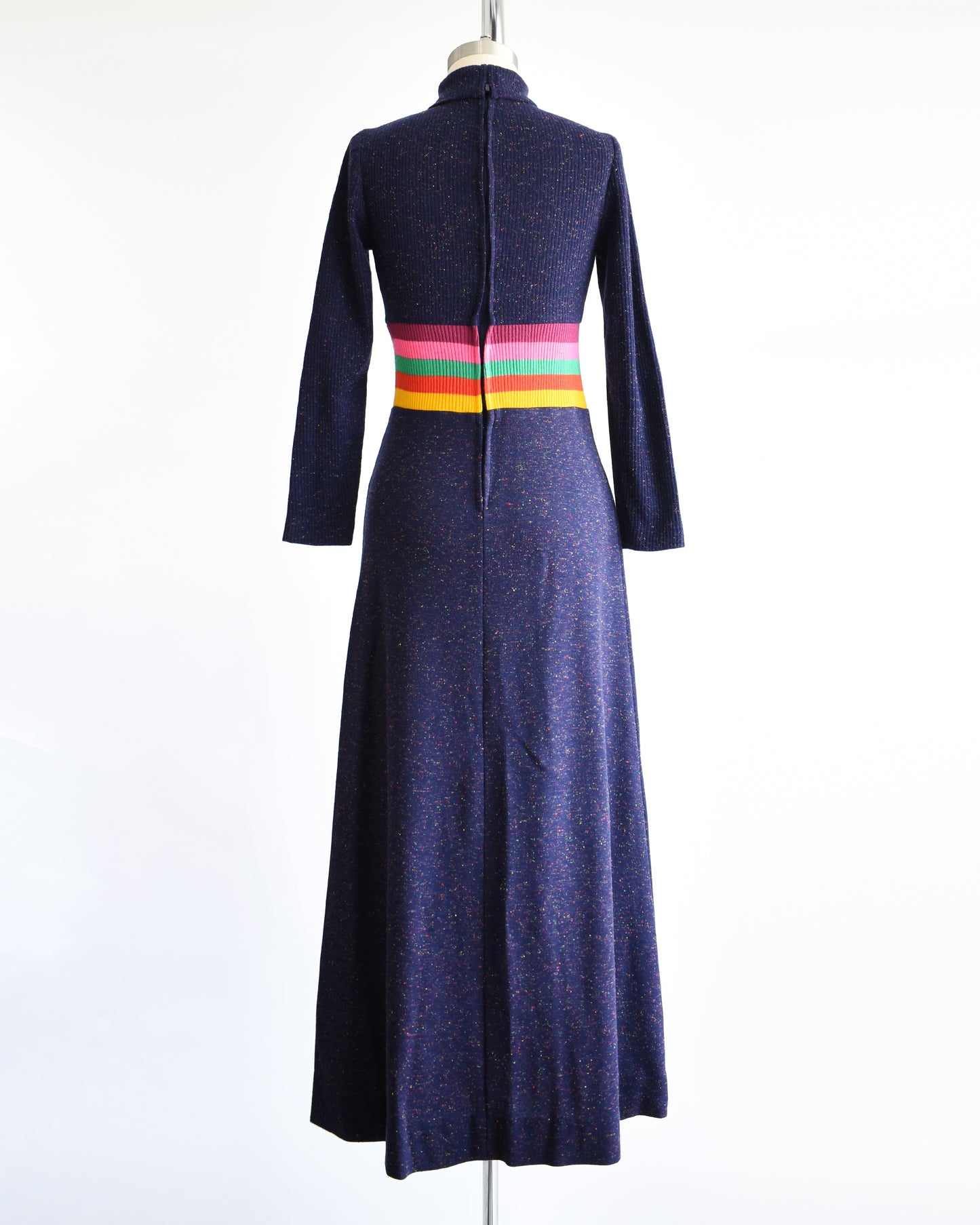 back view of a vintage 1970s purple blue dress with a colorful striped waistband on a mannequin against a white background