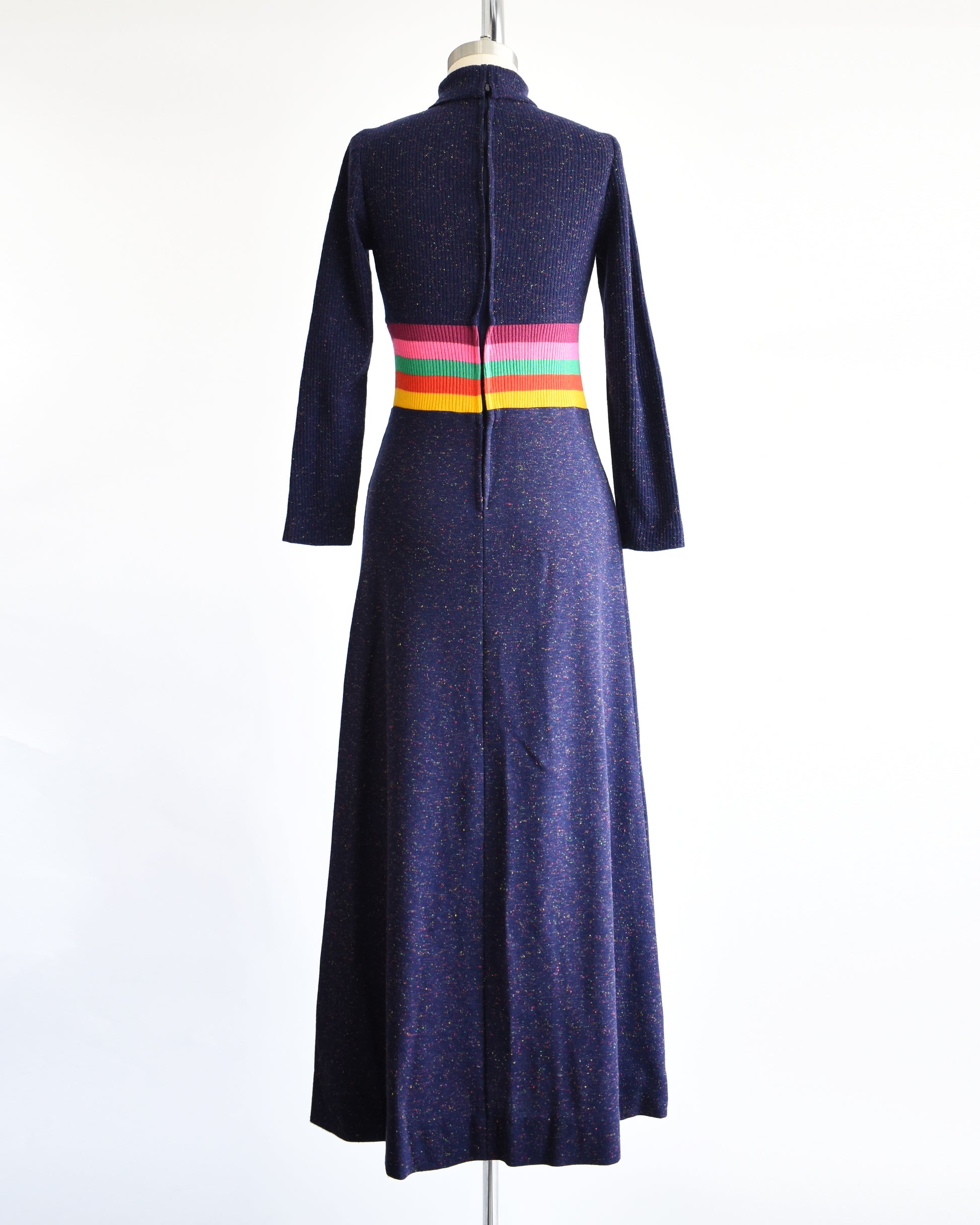 back view of a vintage 1970s purple blue dress with a colorful striped waistband on a mannequin against a white background