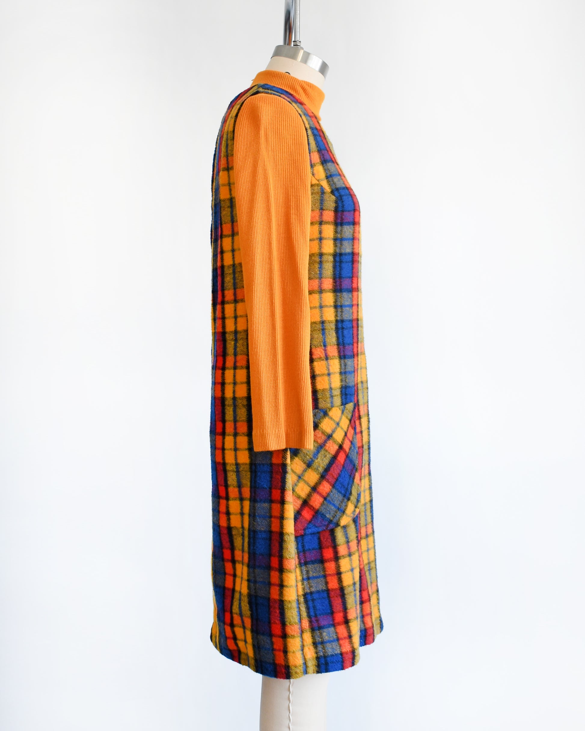 side view of a vintage 1970s orange, blue, and red plaid pinafore dress with an orange turtleneck underneath