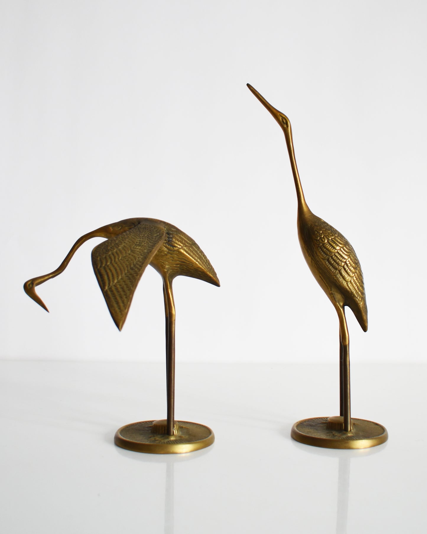 Side view of a  pair of vintage brass cranes that have ornate carved detail on their wings and body.