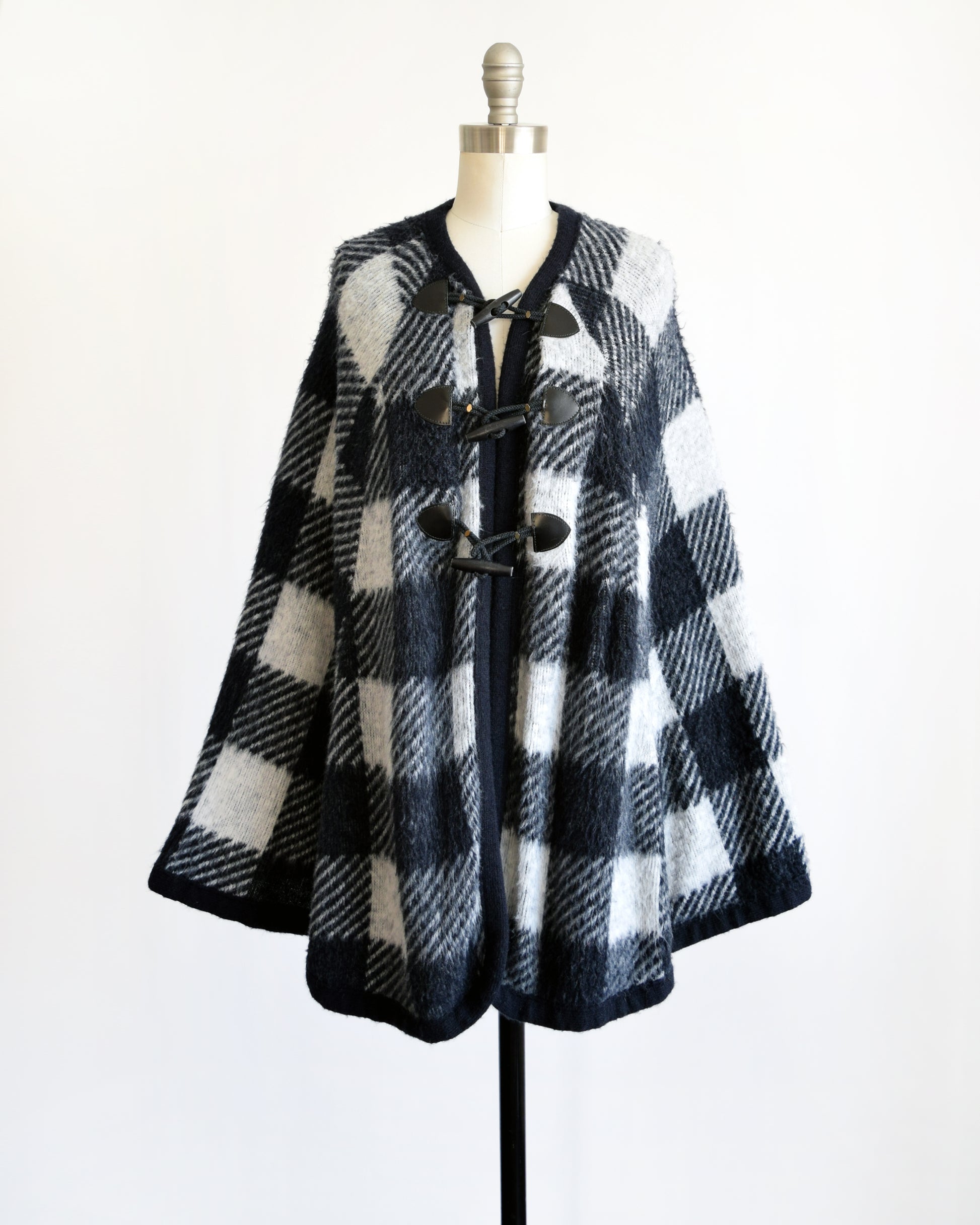 A vintage 1970s black and white plaid poncho with three toggle buttons on the front.