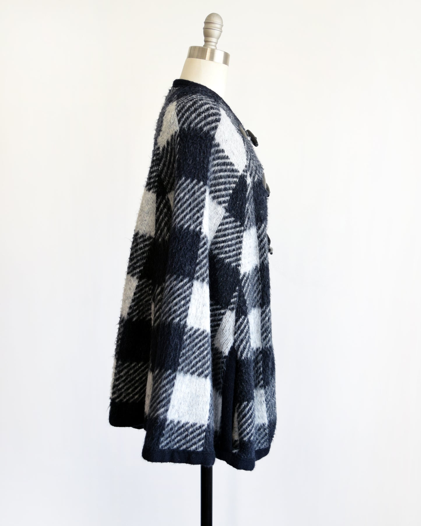 Side view of a vintage 1970s black and white plaid poncho with three toggle buttons on the front.