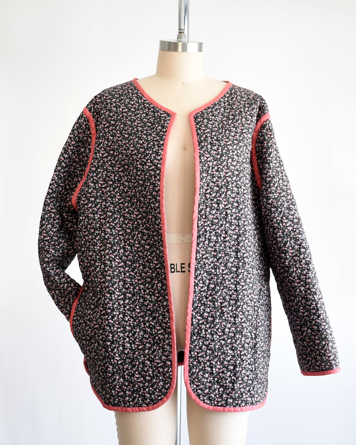 the same jacket but reversed, which shows the vintage 1970s/1980s dark floral quilted jacket with pink trim on a mannequin on a dress form