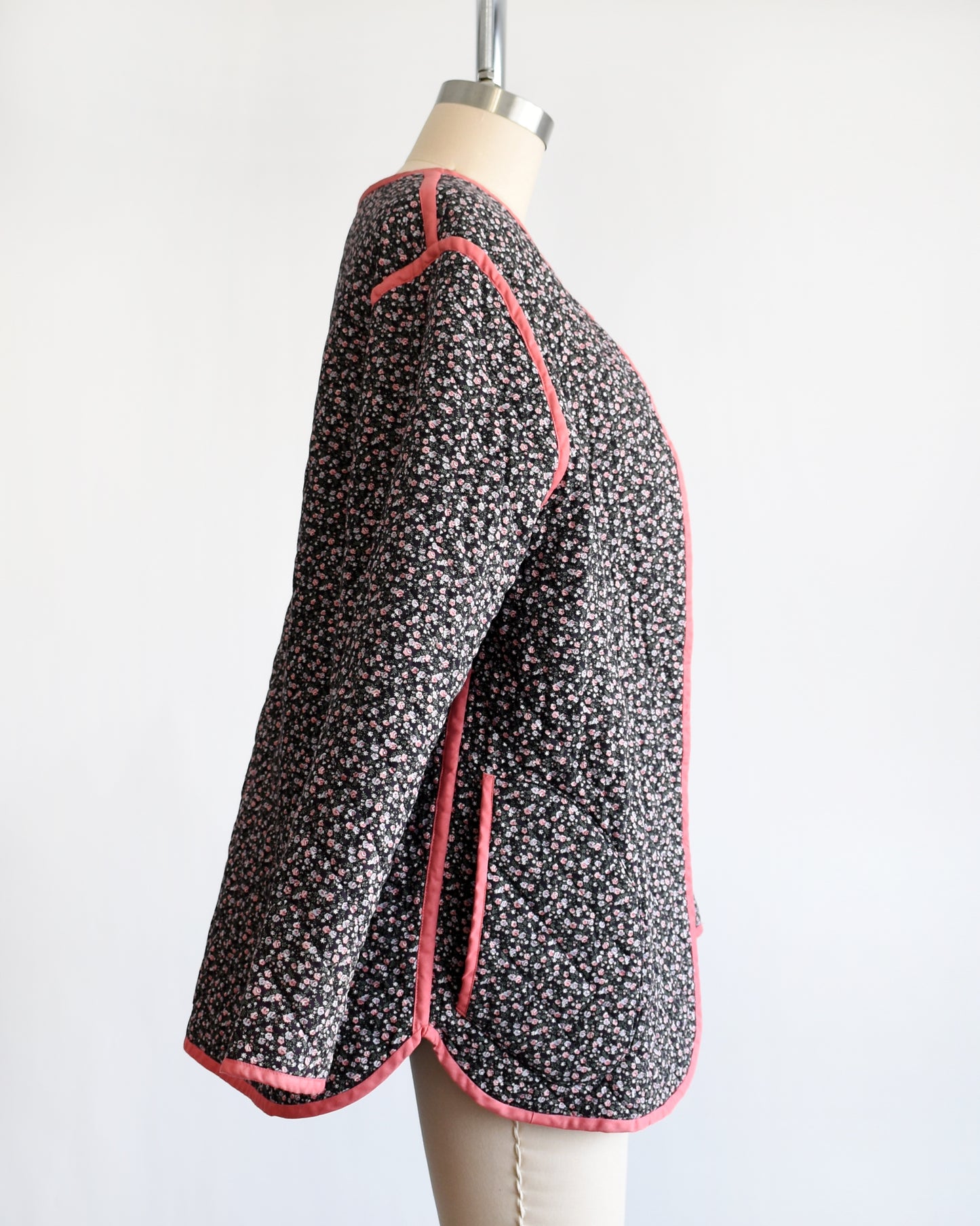 side view of the same jacket but reversed, which shows the vintage 1970s/1980s dark floral quilted jacket with pink trim on a mannequin on a dress form