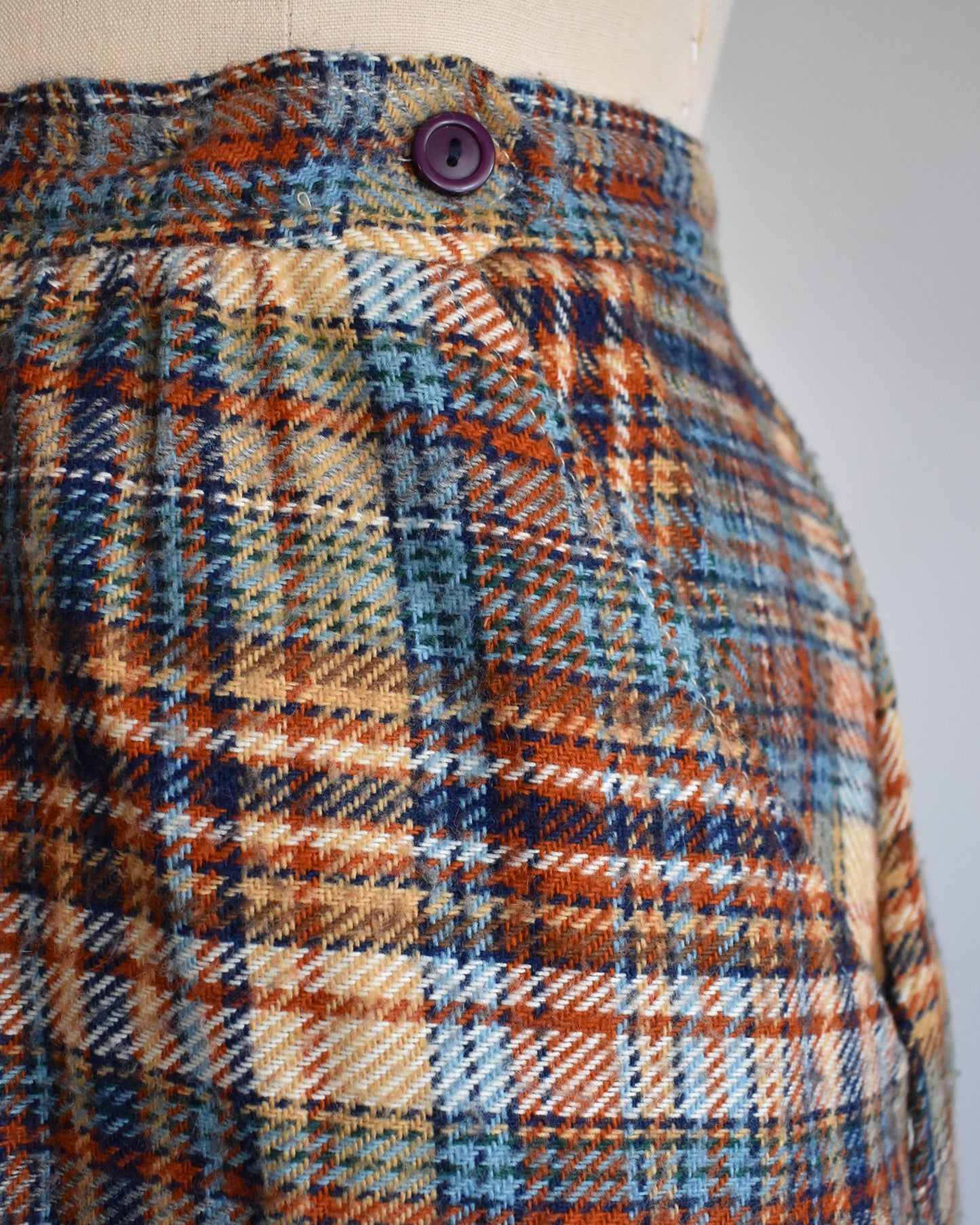 close up of the side button and pocket on a vintage 1970s brown and blue plaid skirt on a dress form against a white background