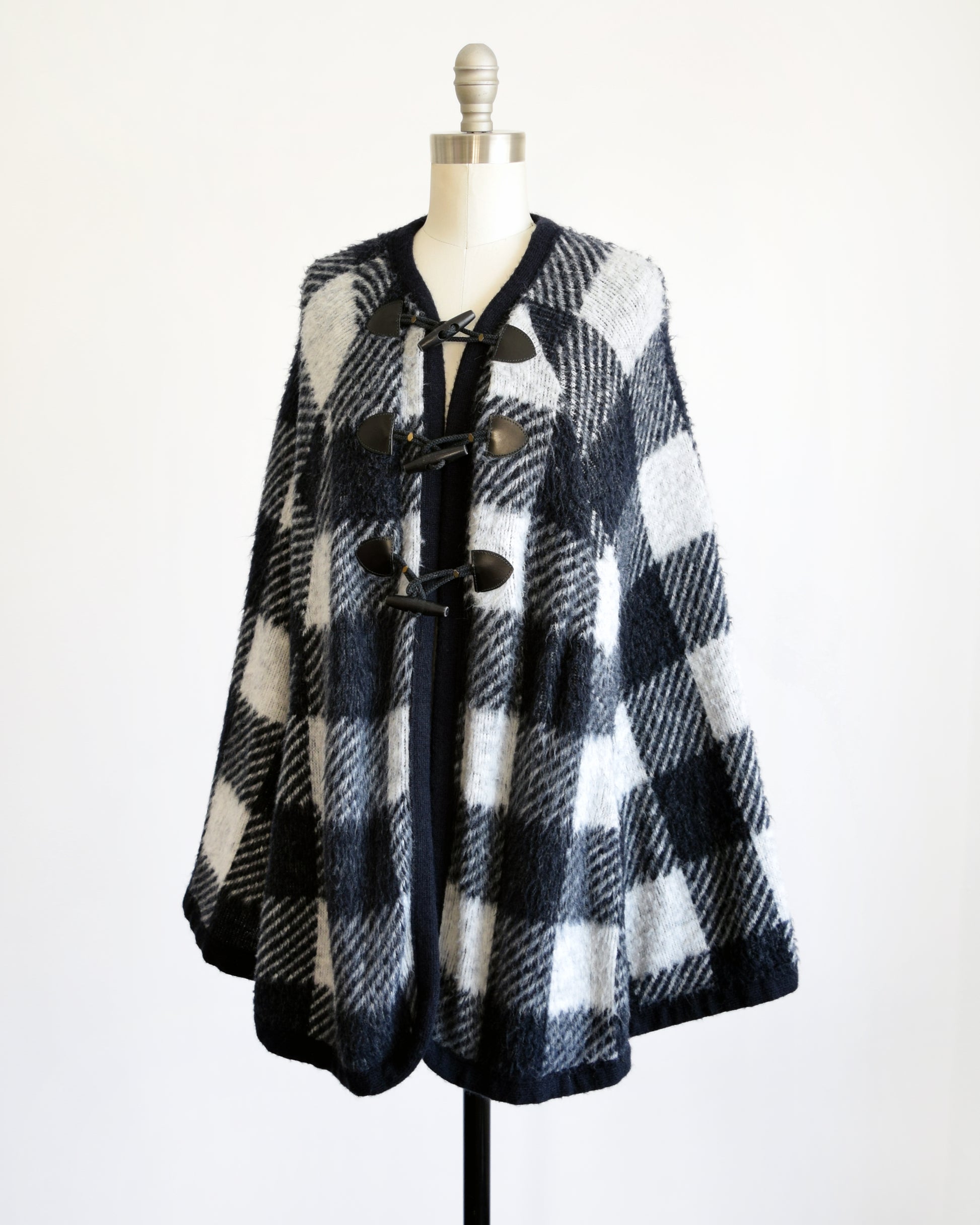 Side front view of a vintage 1970s black and white plaid poncho with three toggle buttons on the front.