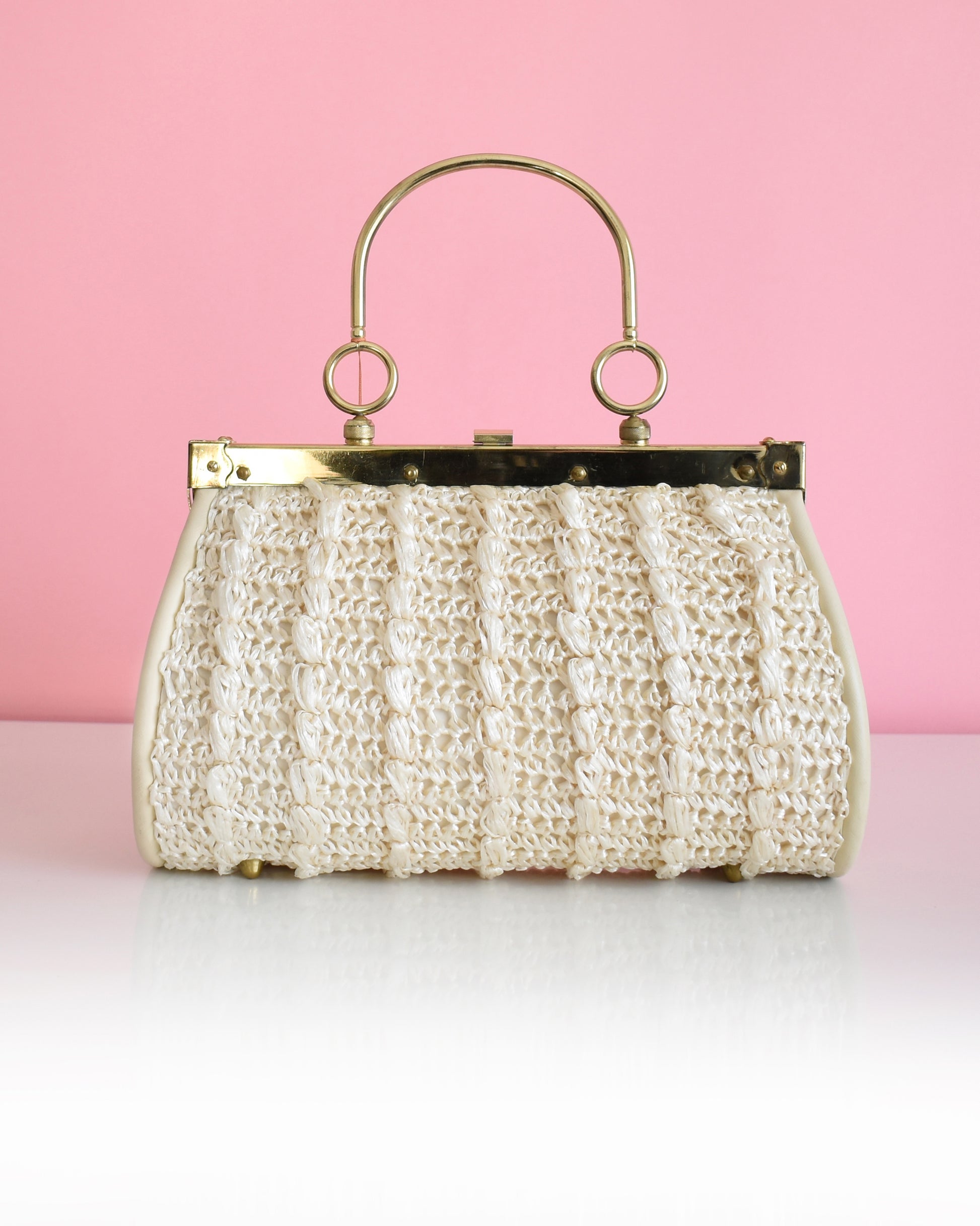 a vintage 1960s white woven handbag with gold frame and handle against a pink background