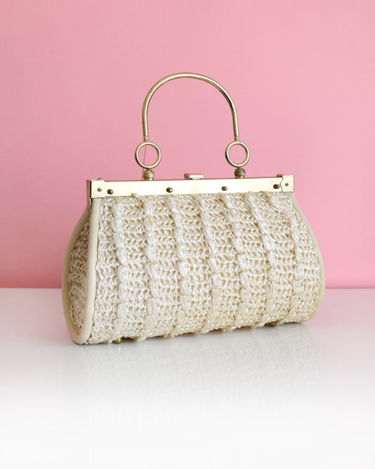 a vintage 1960s white woven handbag with gold frame and handle against a pink background