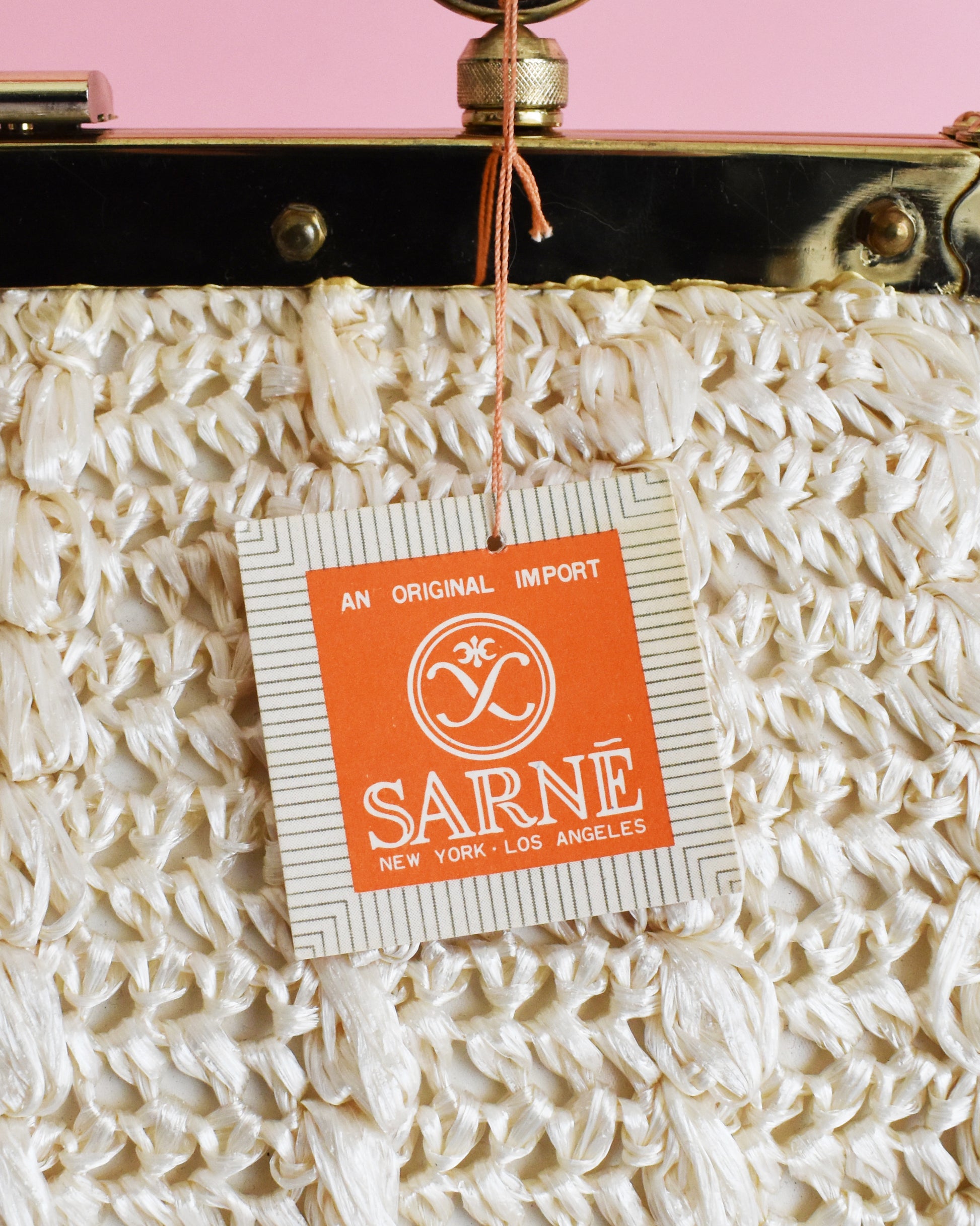 Vintage handbag with a SARNE label tag on a pink background