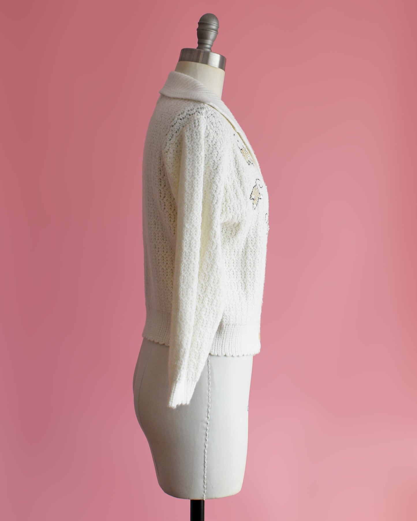 side view of a vintage white cardigan with embroidered details on a mannequin against a pink background