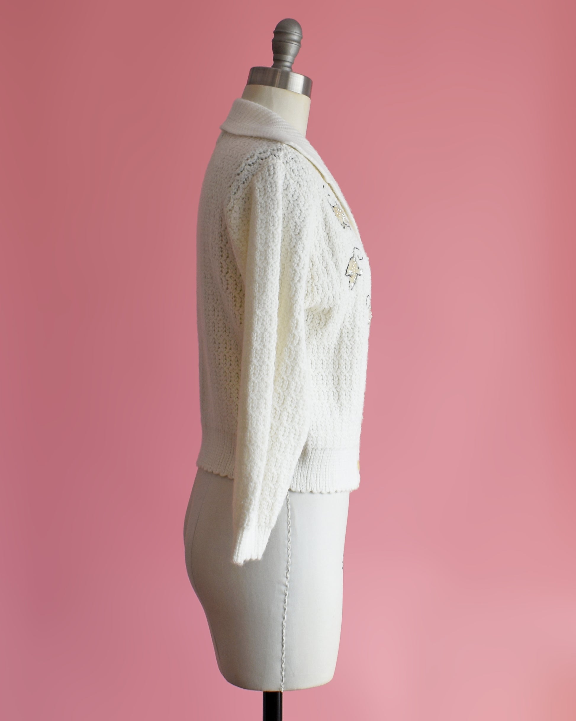 side view of a vintage white cardigan with embroidered details on a mannequin against a pink background