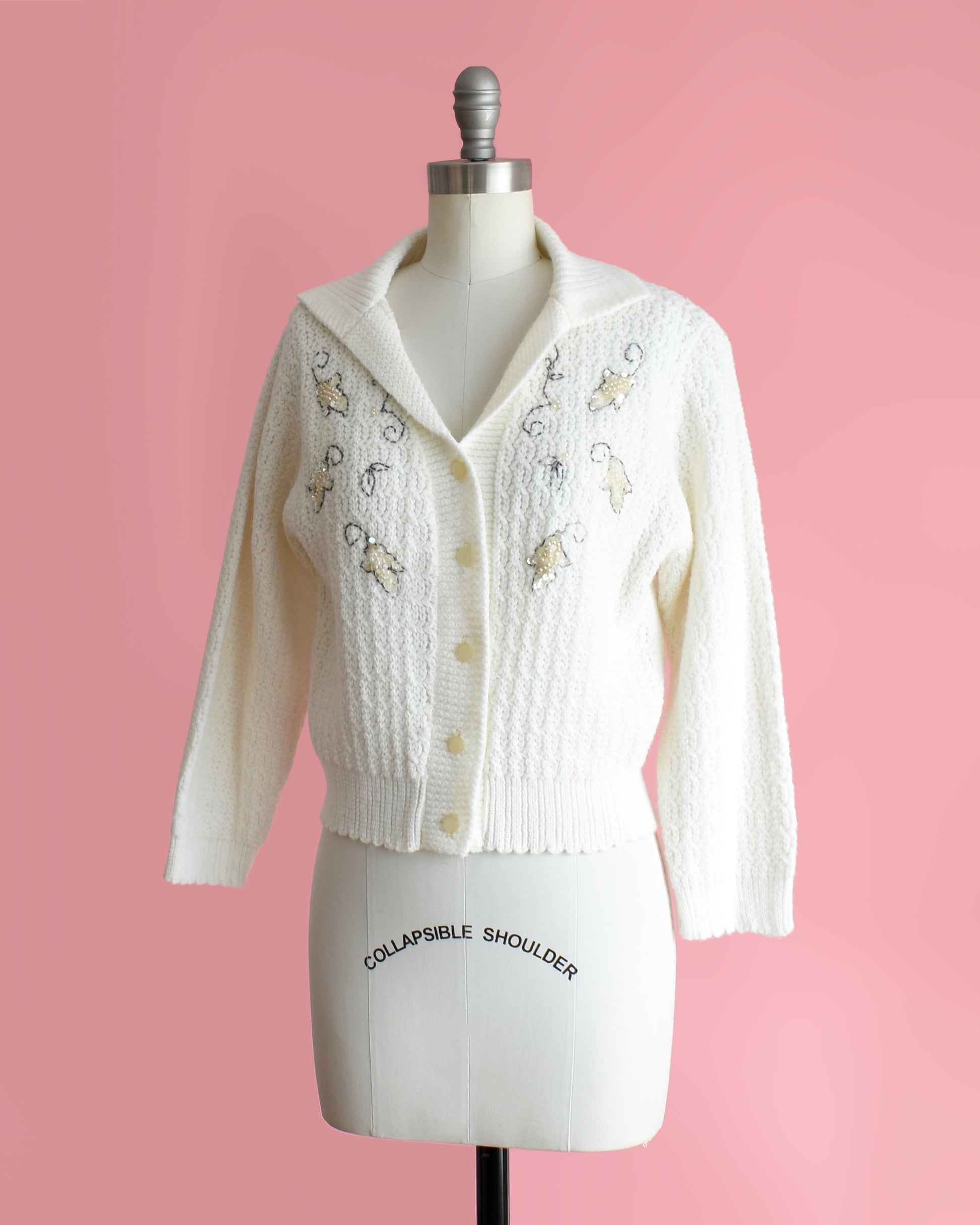 side front view of a vintage white cardigan with embroidered details on a mannequin against a pink background