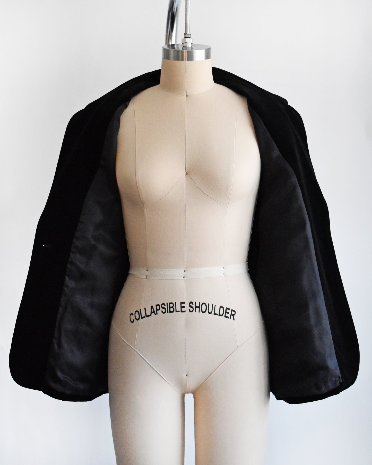 a vintage black blazer that's opening showing the black lining on a mannequin against a white background