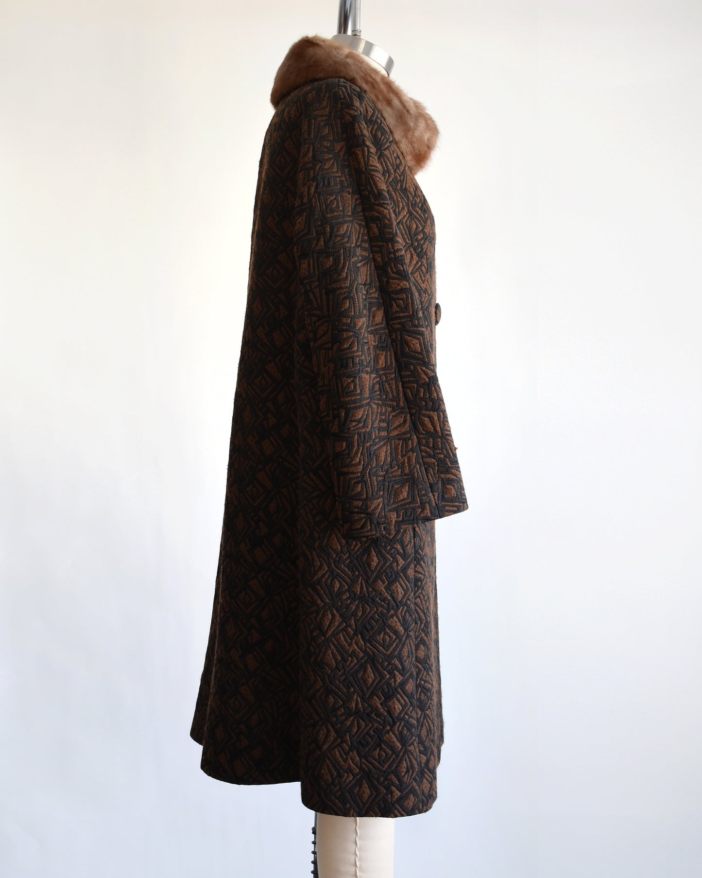 side view of a vintage 1960s black and brown fur collar coat on a dress form against a white background