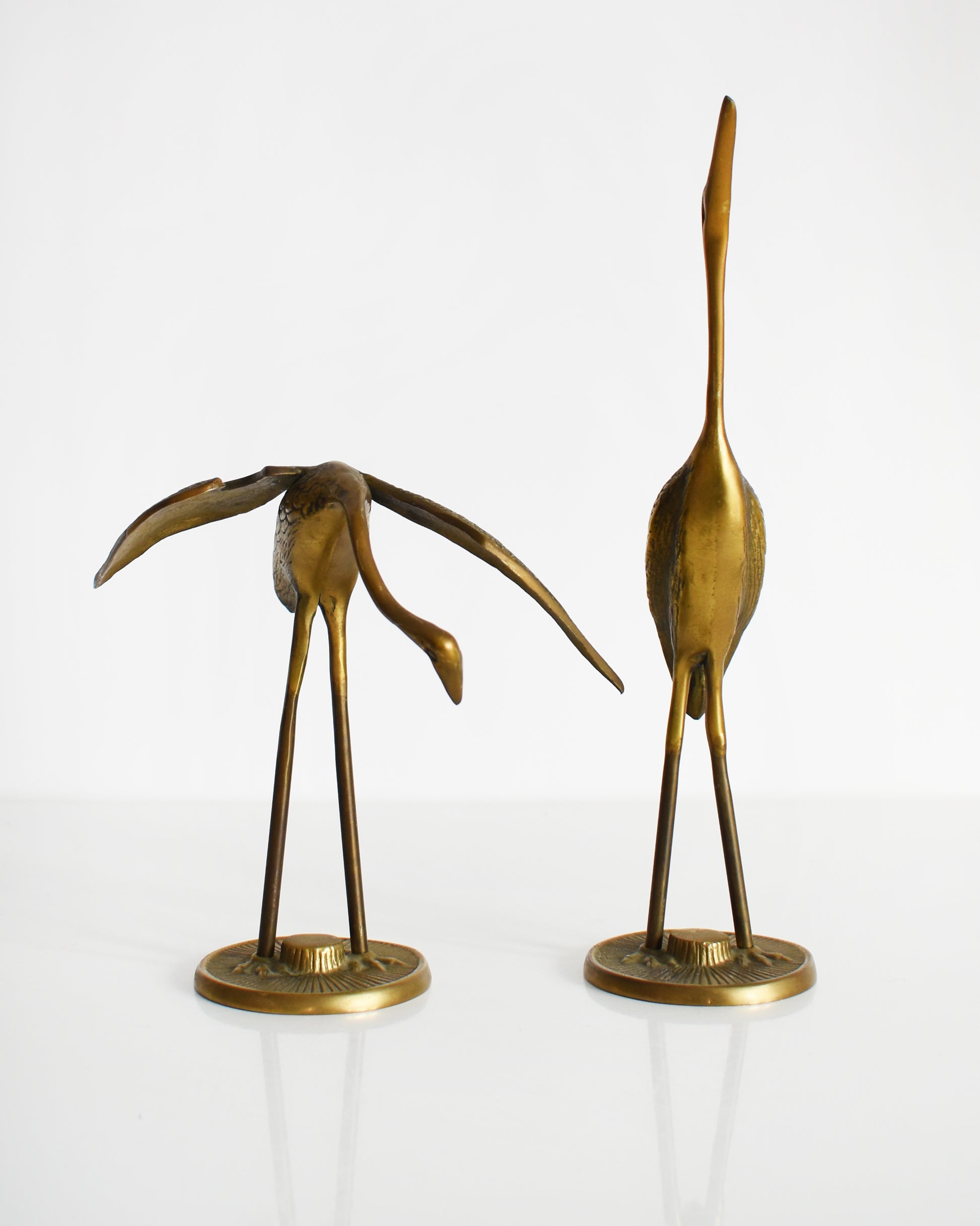 Front view of a pair of vintage brass cranes that have ornate carved detail on their wings and body.