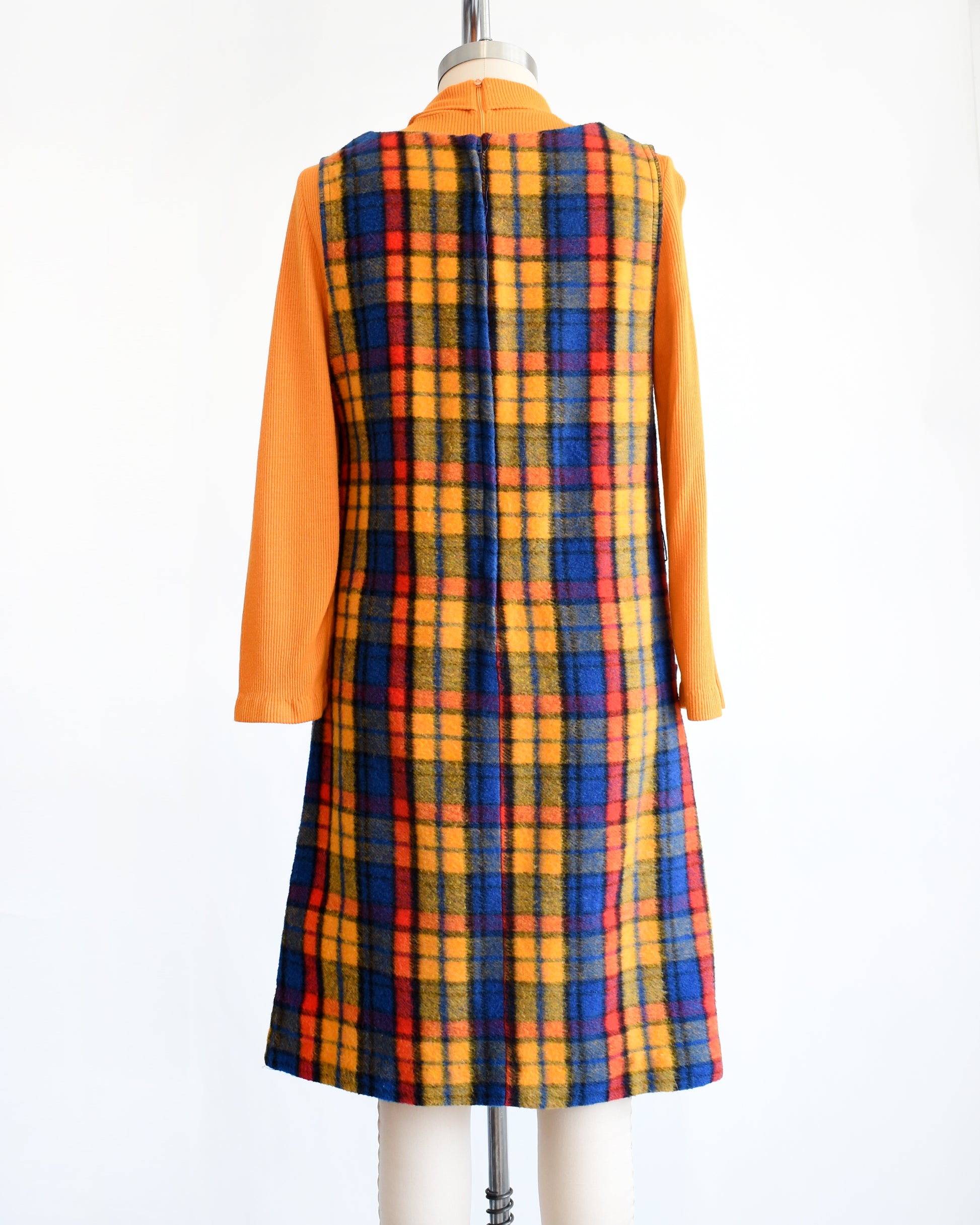 back view of a vintage 1970s orange, blue, and red plaid pinafore dress with an orange turtleneck underneath