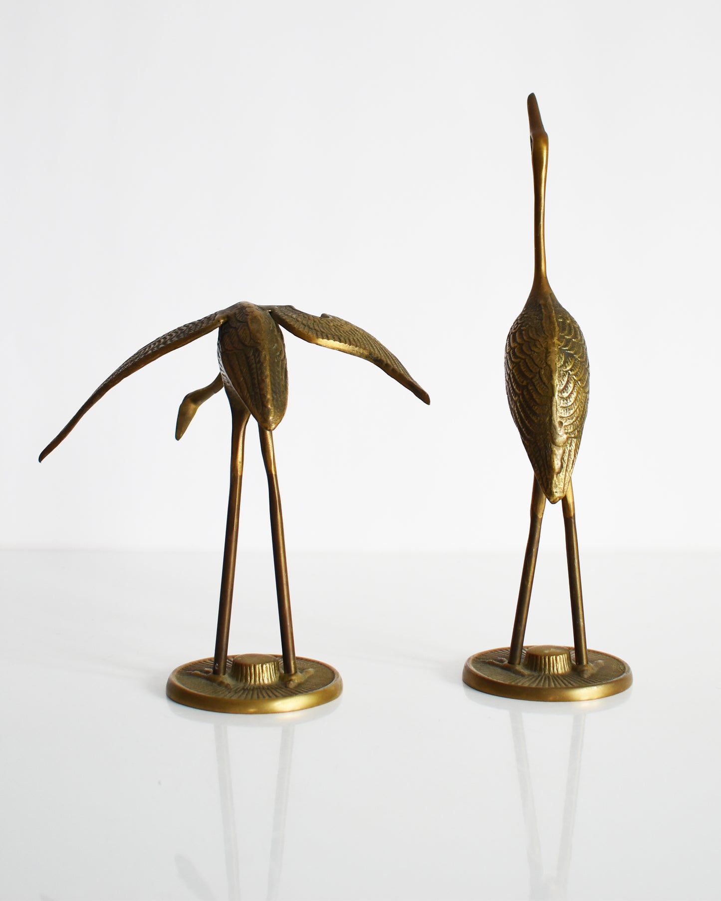 Back view of a pair of vintage brass cranes that have ornate carved detail on their wings and body.