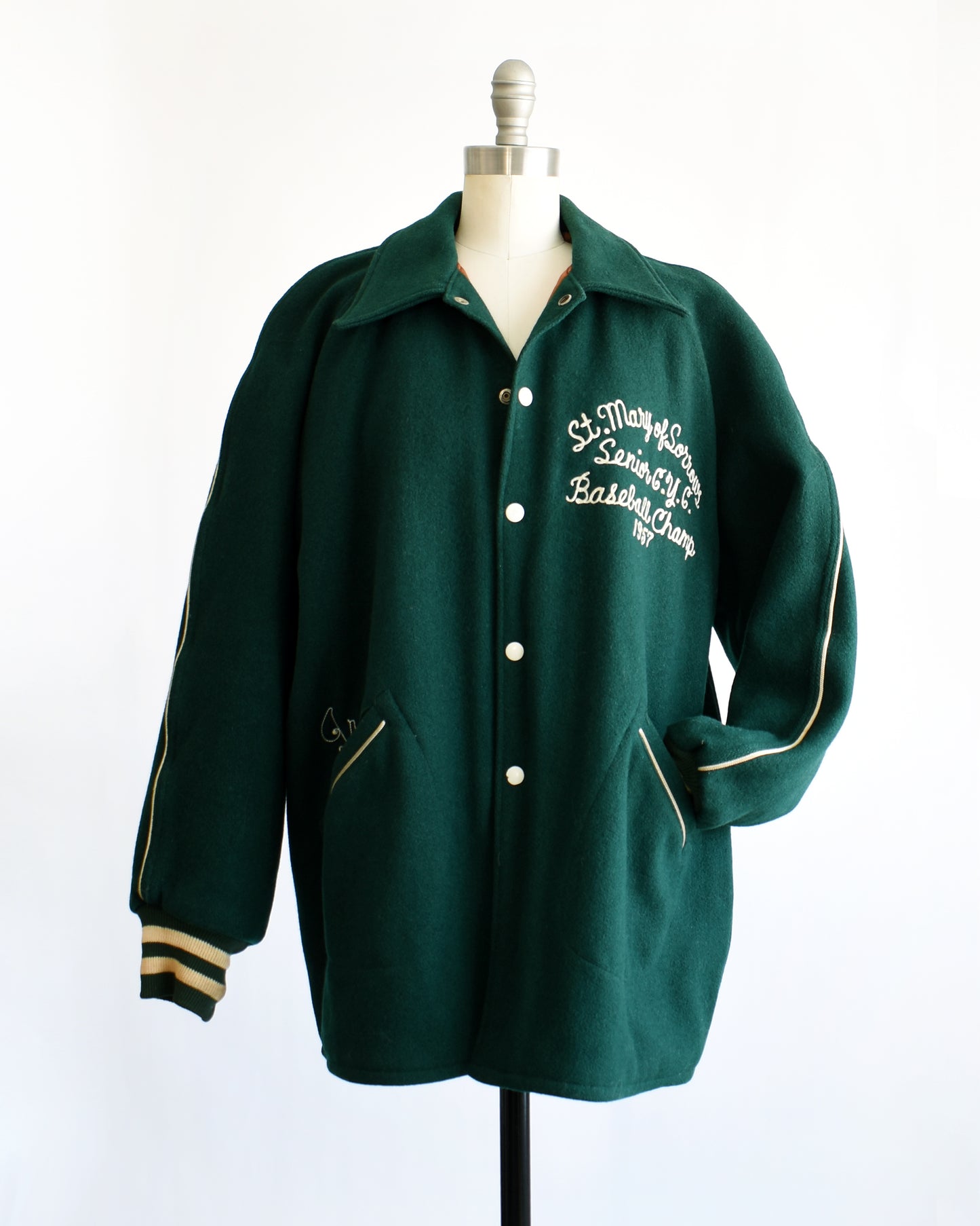 a vintage 1950s green varsity jacket with white text on a mannequin against a white background