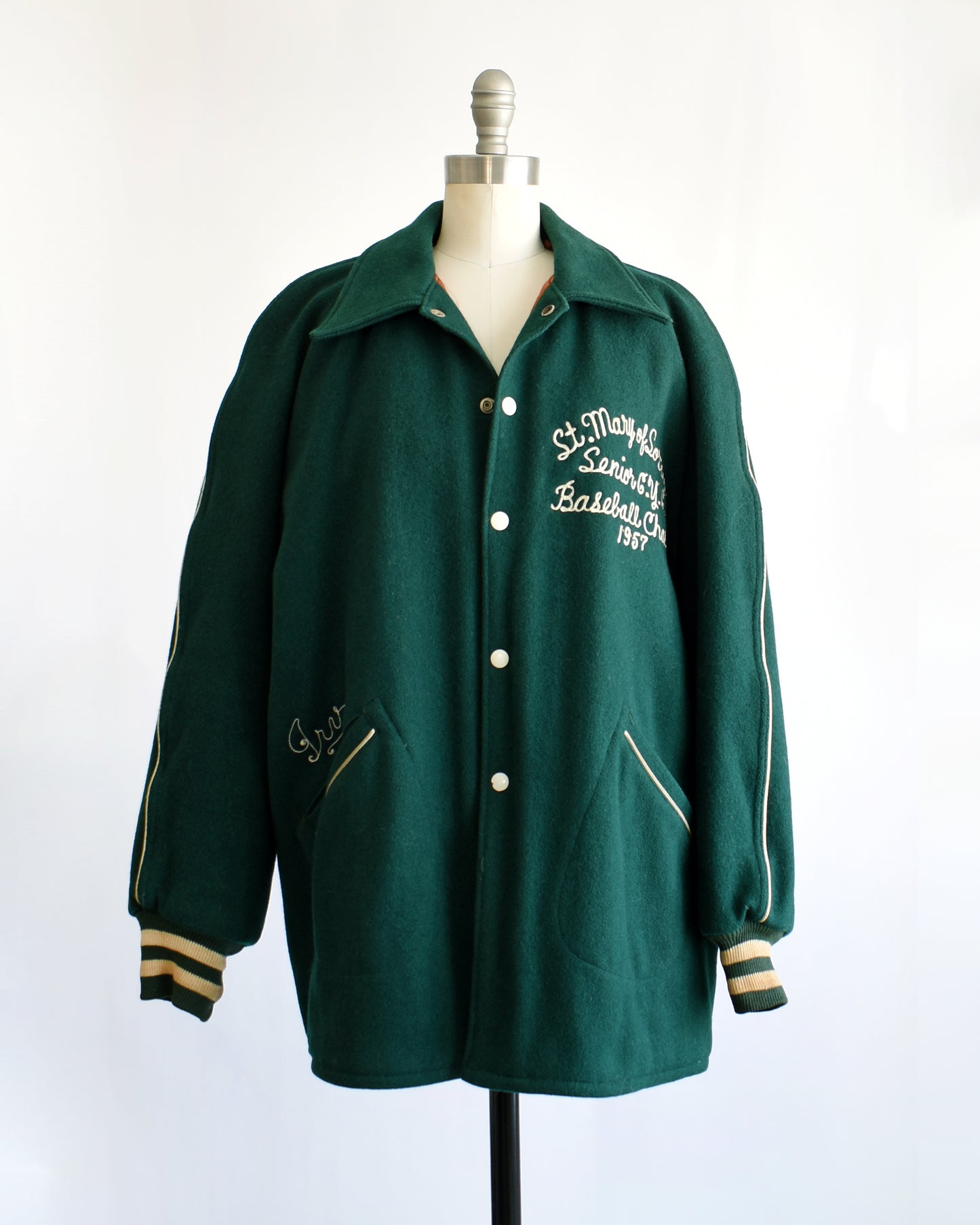 a vintage 1950s green varsity jacket with white text on a mannequin against a white background