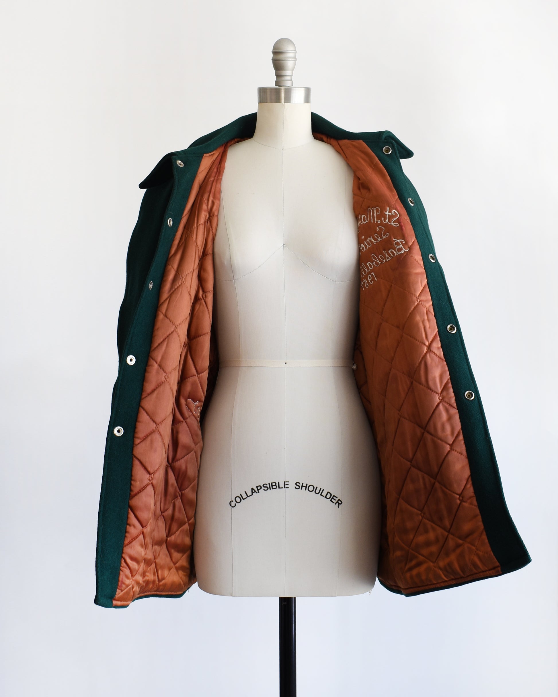 a vintage 1950s green varsity jacket that's opening showing the quilted lining on a mannequin against a white background