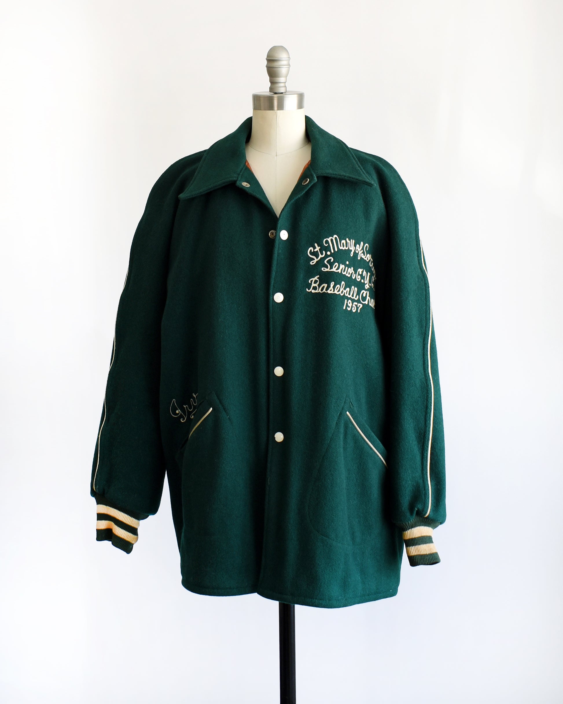 side front view of a vintage 1950s green varsity jacket with white text on a mannequin against a white background