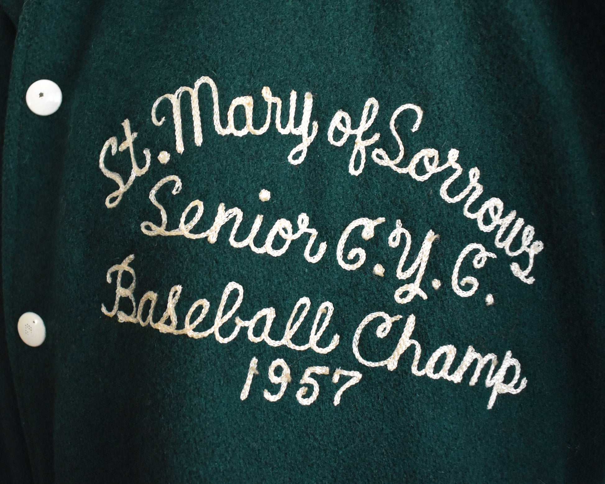 Green jacket with embroidered text 'St. Mary of Sorrows Senior C.Y.C. Baseball Champ 1957' on a dark background