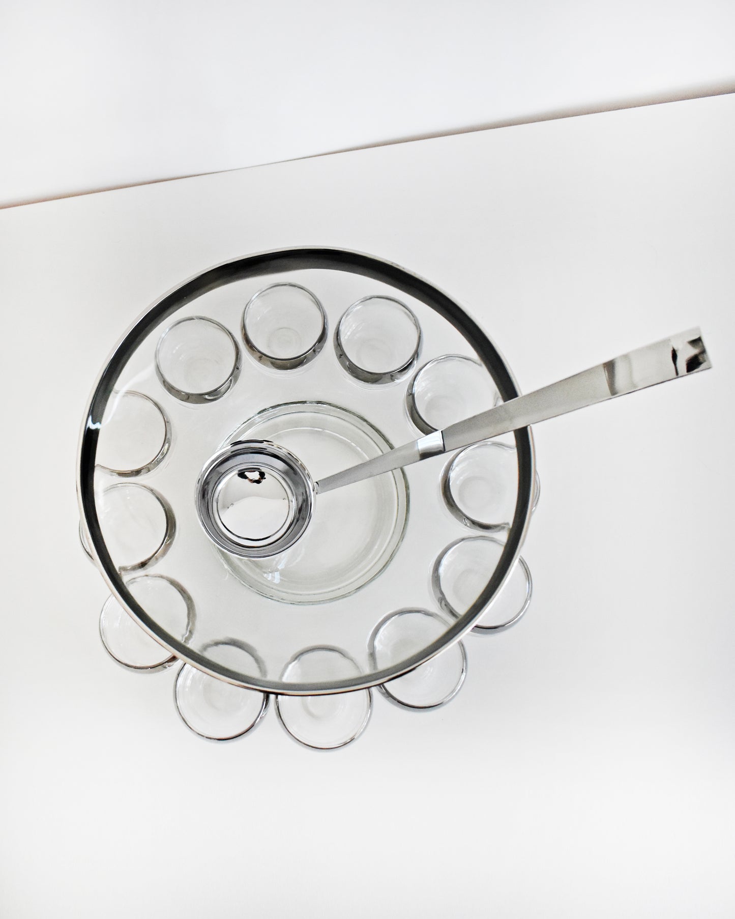 overhead shot of a vintage 1960s silver rim punch bowl set with ladle on a white background