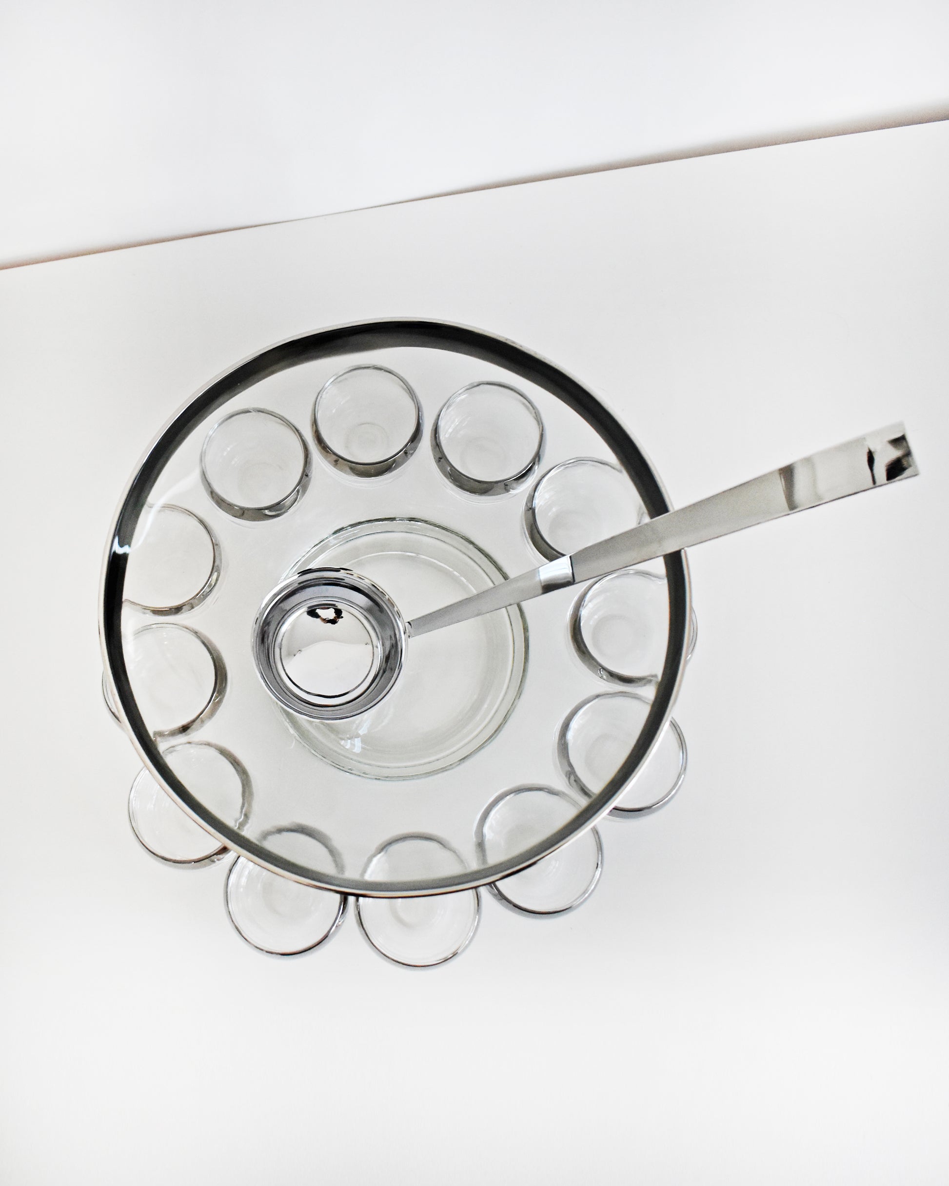 overhead shot of a vintage 1960s silver rim punch bowl set with ladle on a white background