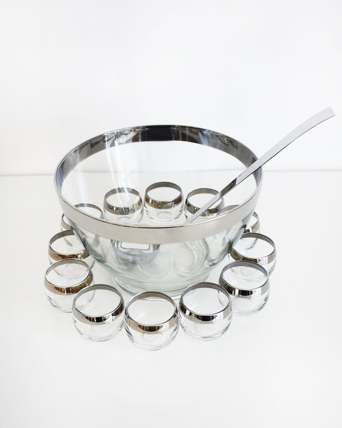 a vintage 1960s silver rim punch bowl set with ladle on a white background