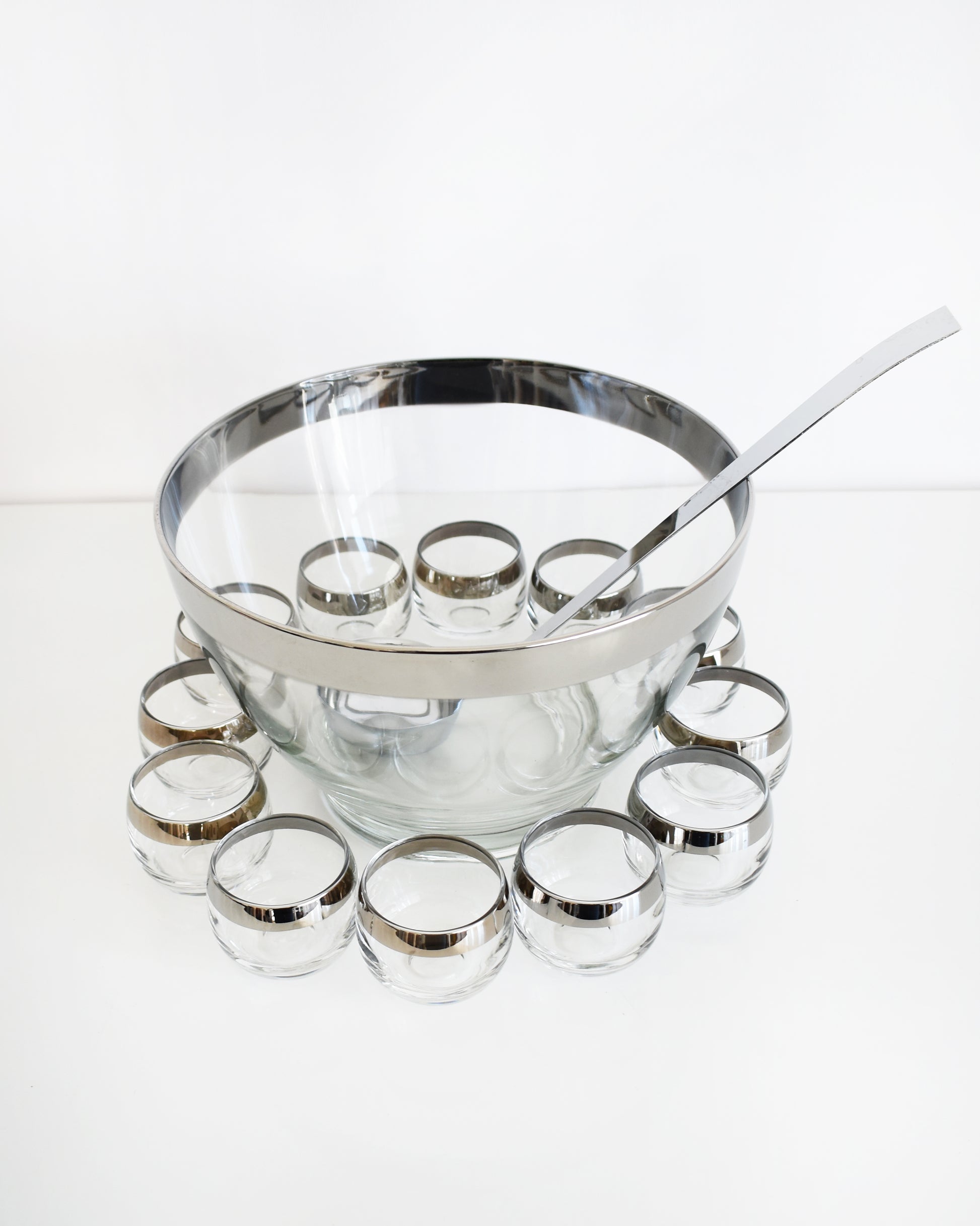a vintage 1960s silver rim punch bowl set with ladle on a white background
