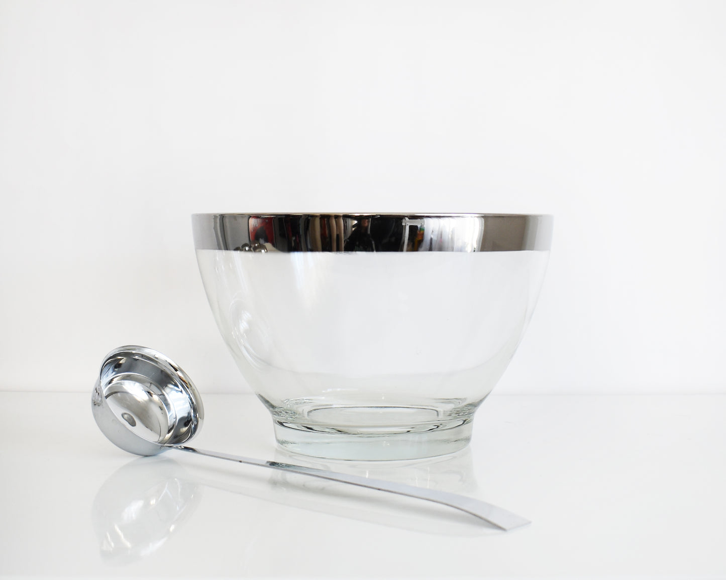 Clear glass bowl with silver rim and matching ladle on a white background