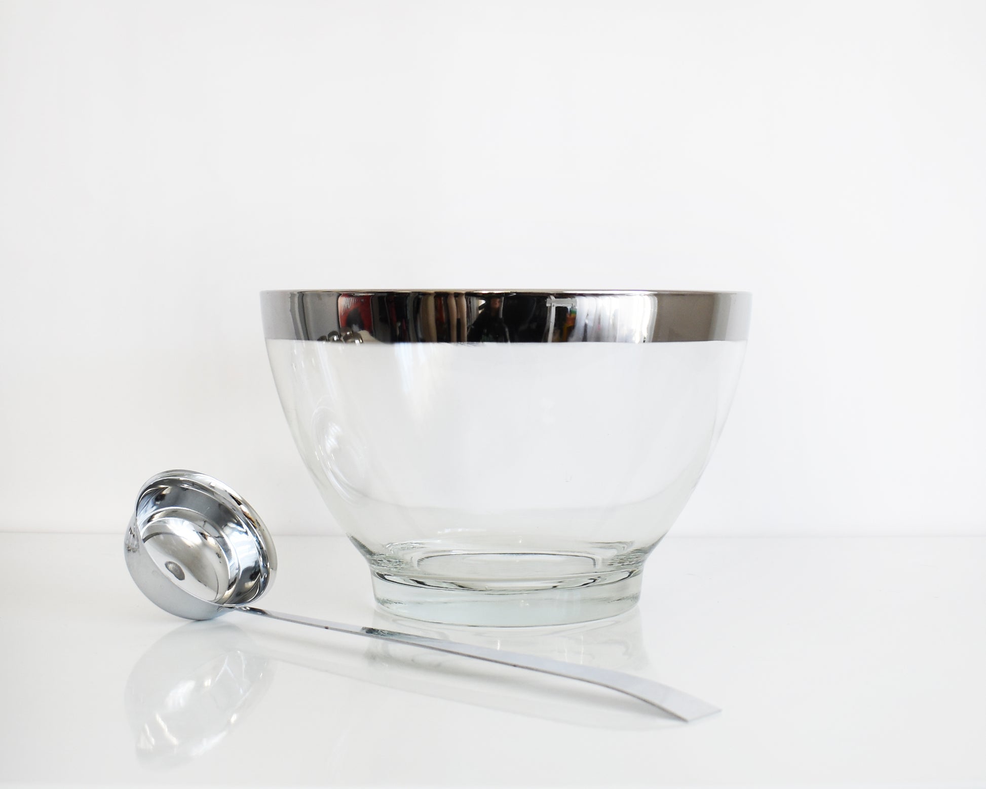 Clear glass bowl with silver rim and matching ladle on a white background