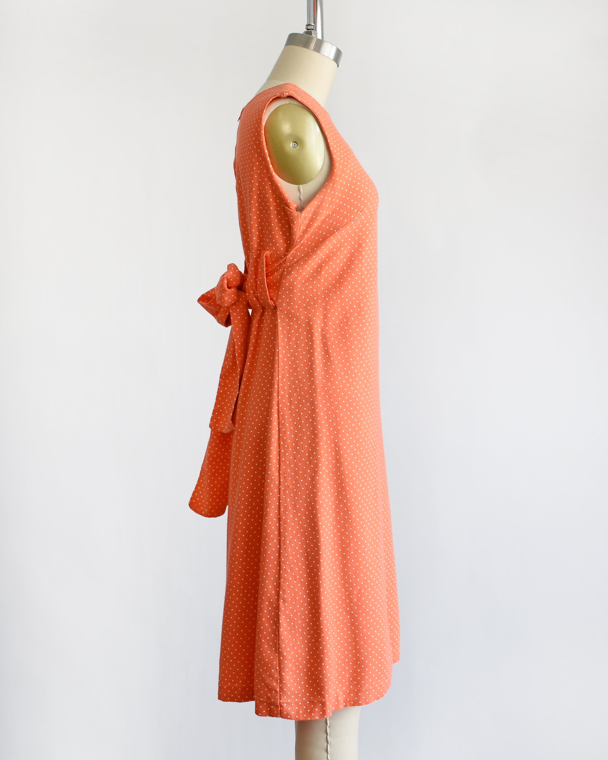 side view of a vintage peach orange polka dot dress on a mannequin against a white background