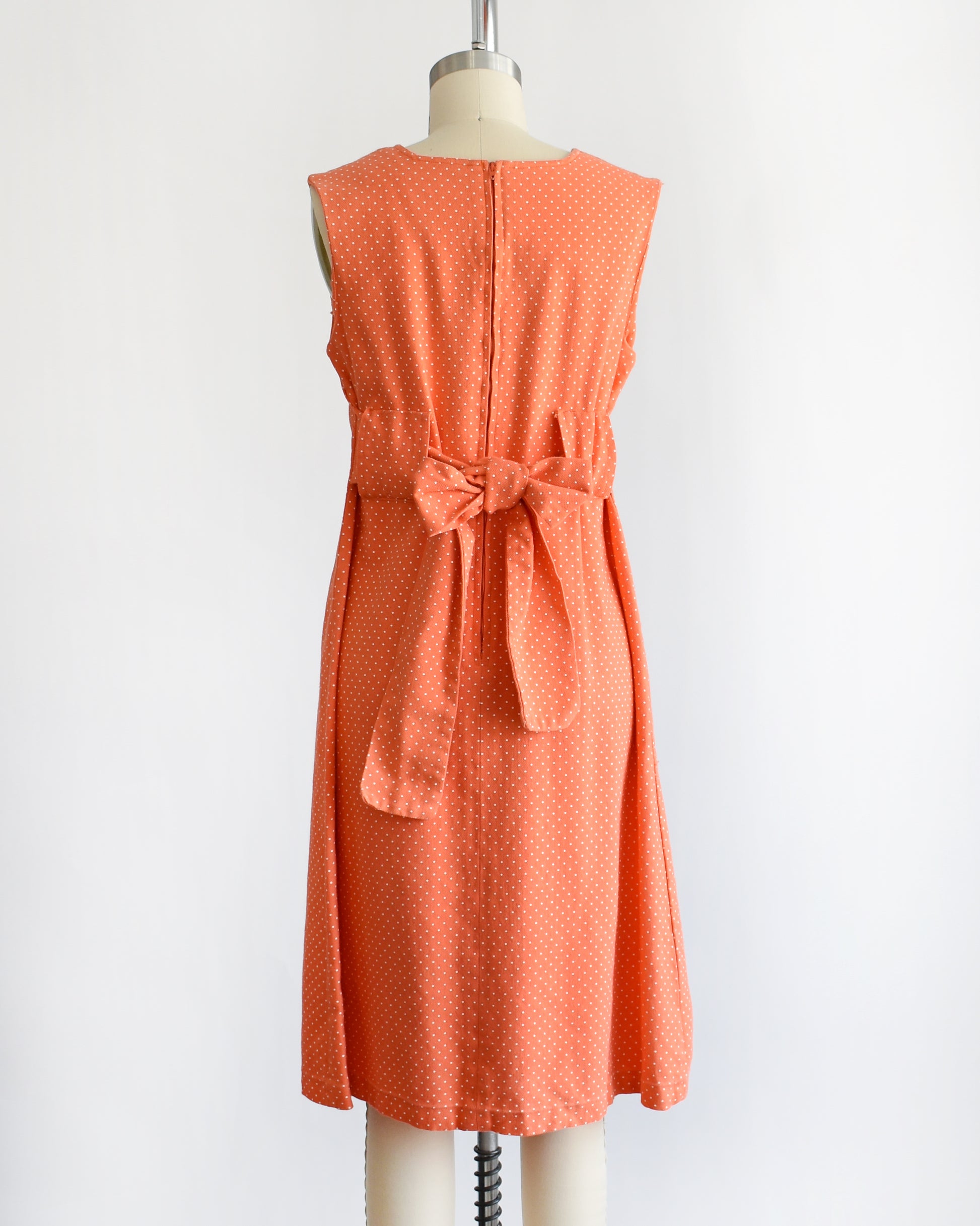 back view of a vintage peach orange polka dot dress on a mannequin against a white background