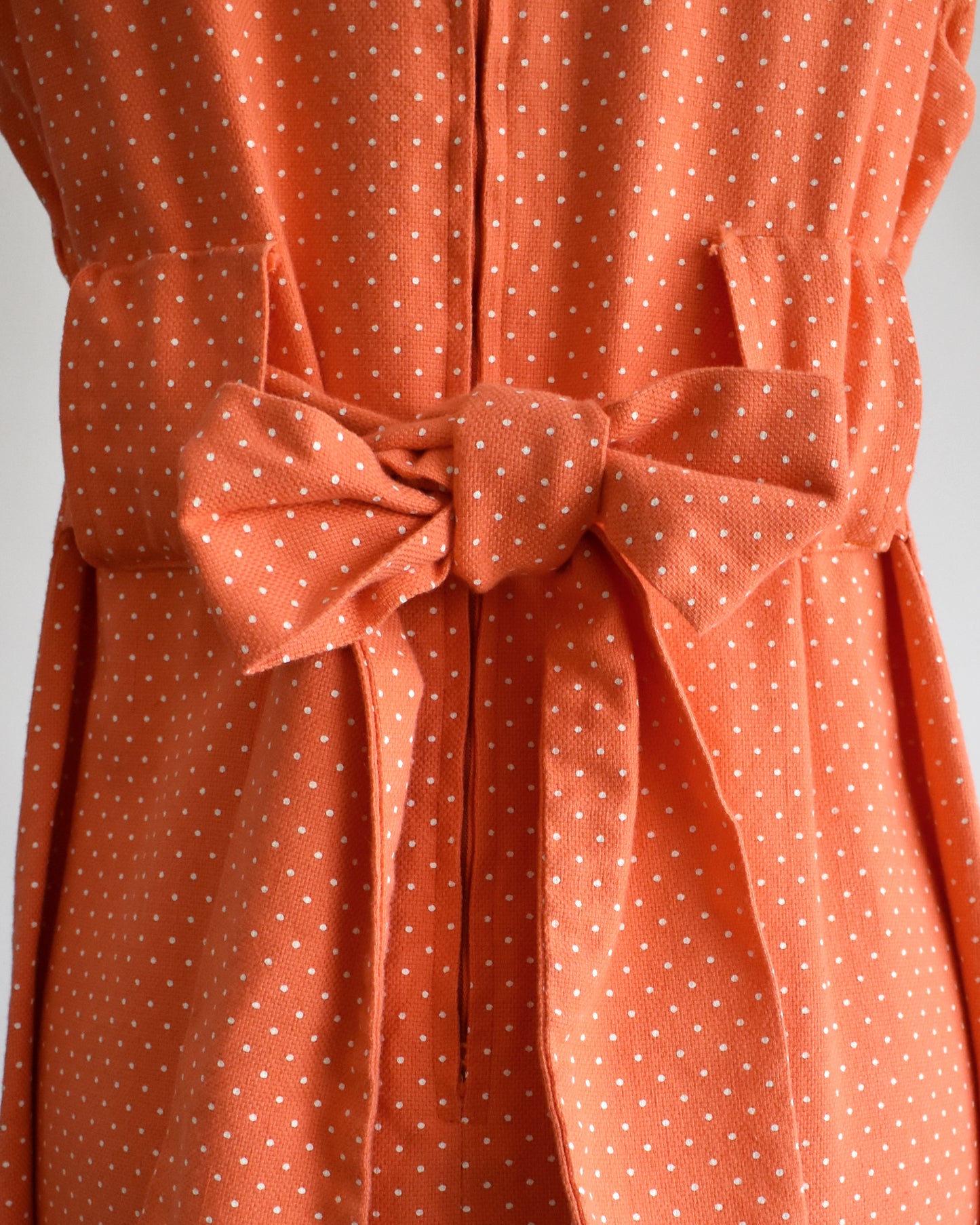 close up of the back bow on a vintage peach orange polka dot dress on a mannequin against a white background