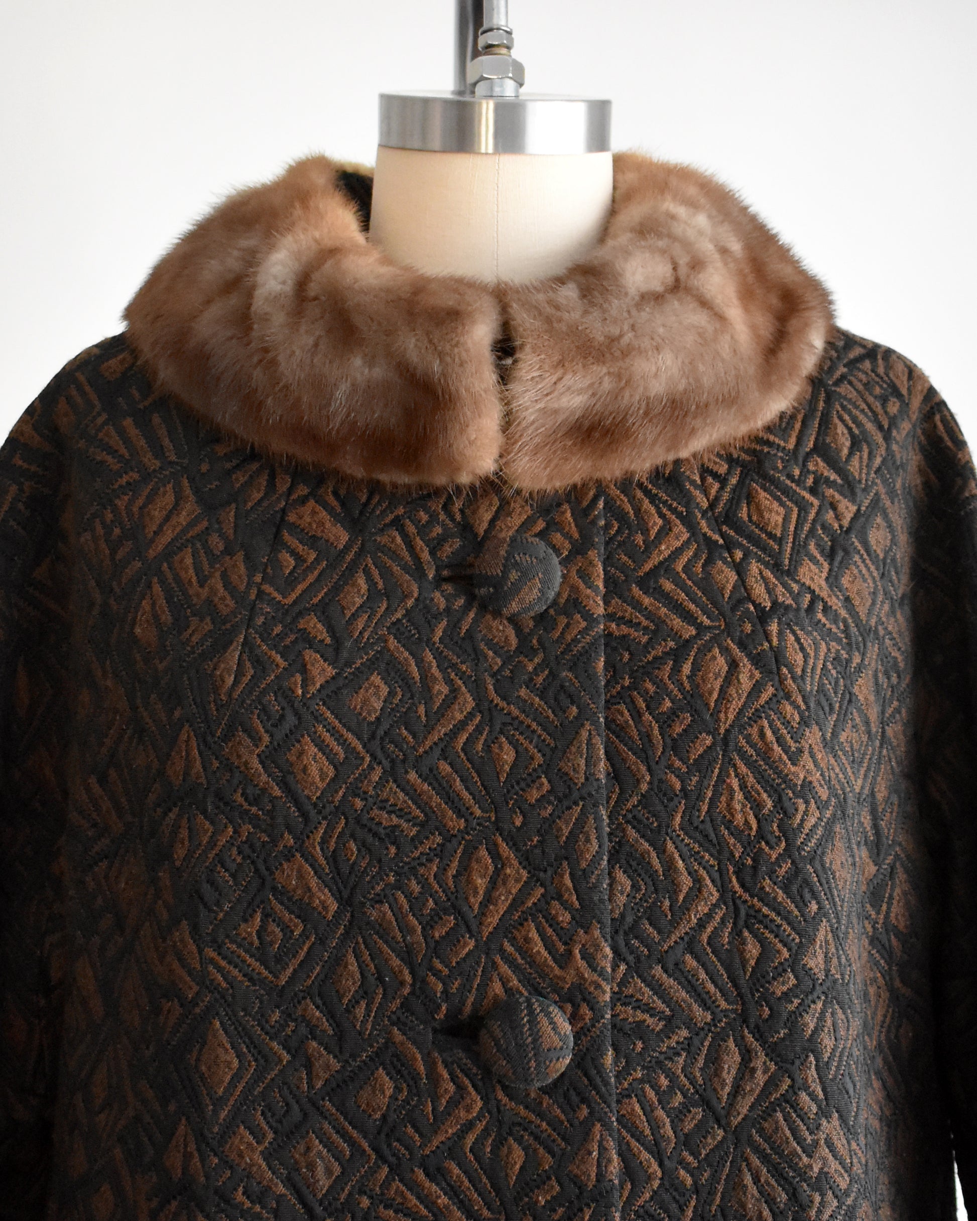 close up of the bodice and fur collar on a vintage 1960s black and brown fur collar coat on a dress form against a white background